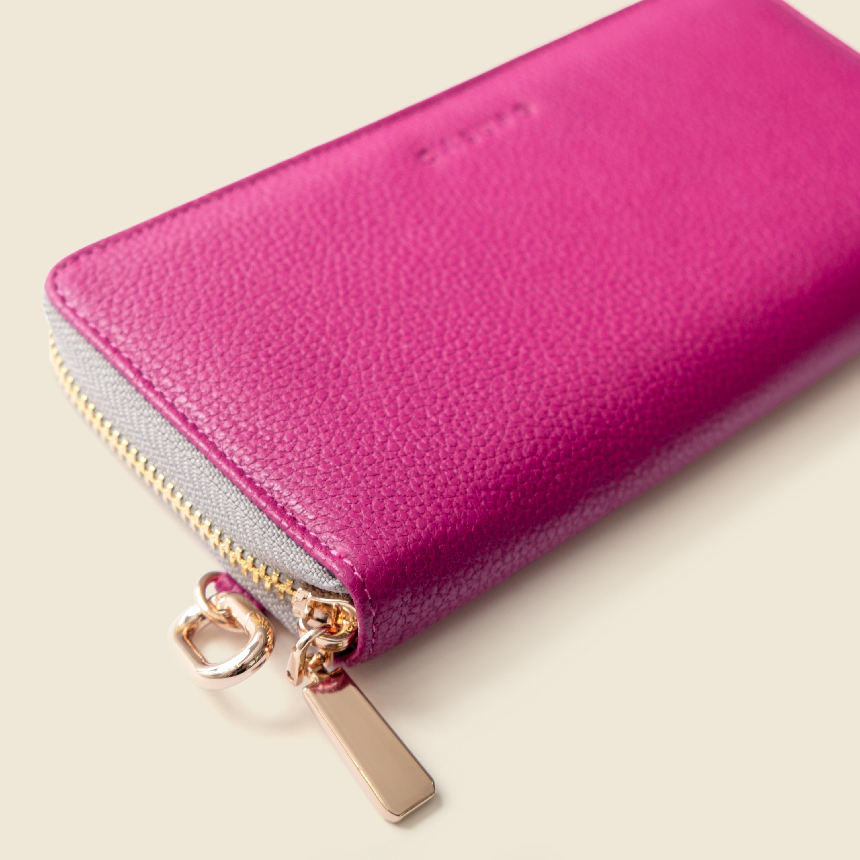 Pink wallet with gold zipper on a light beige background