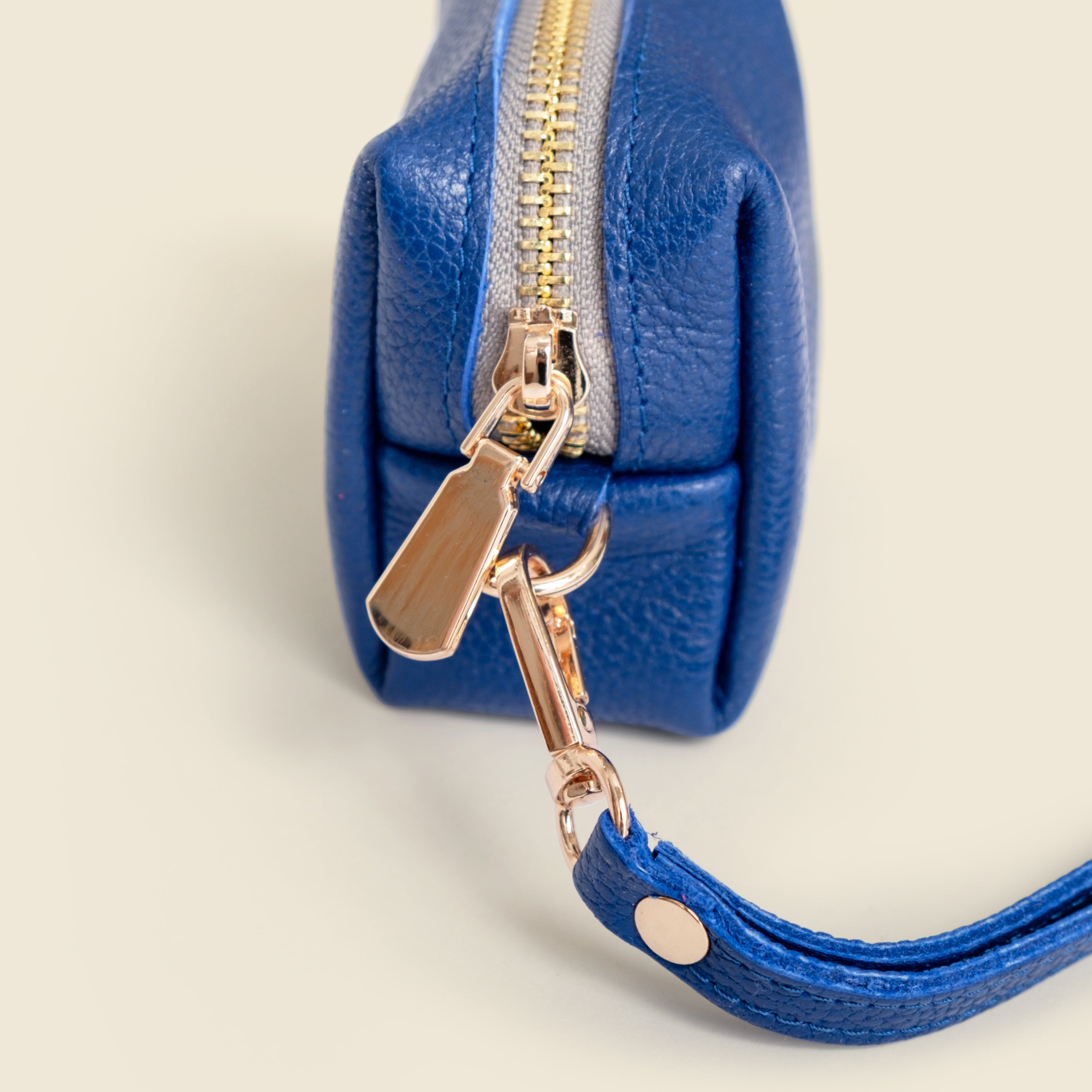 Blue leather pouch with gold zipper and matching strap on a light beige background