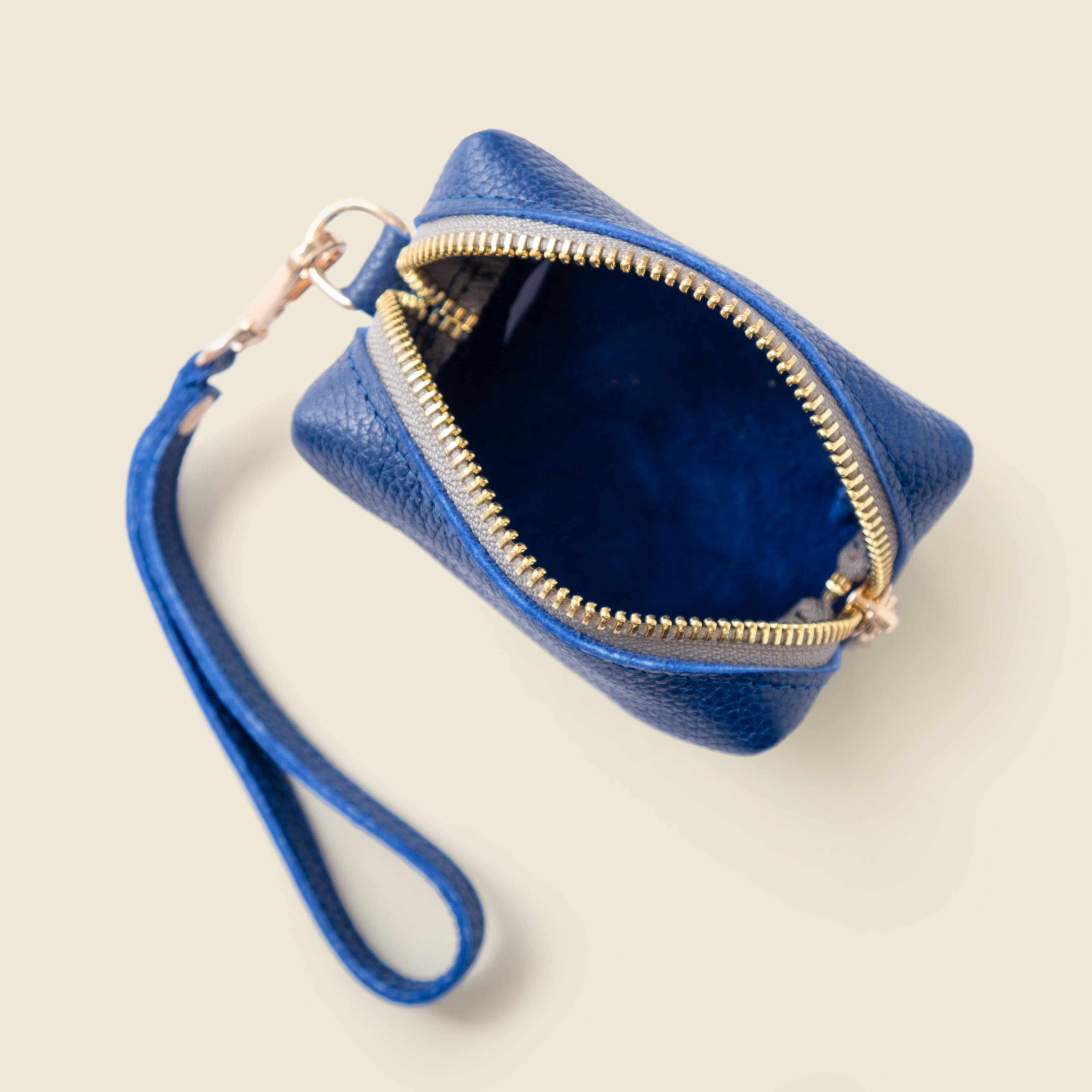 Blue leather wristlet with gold zipper on a beige background
