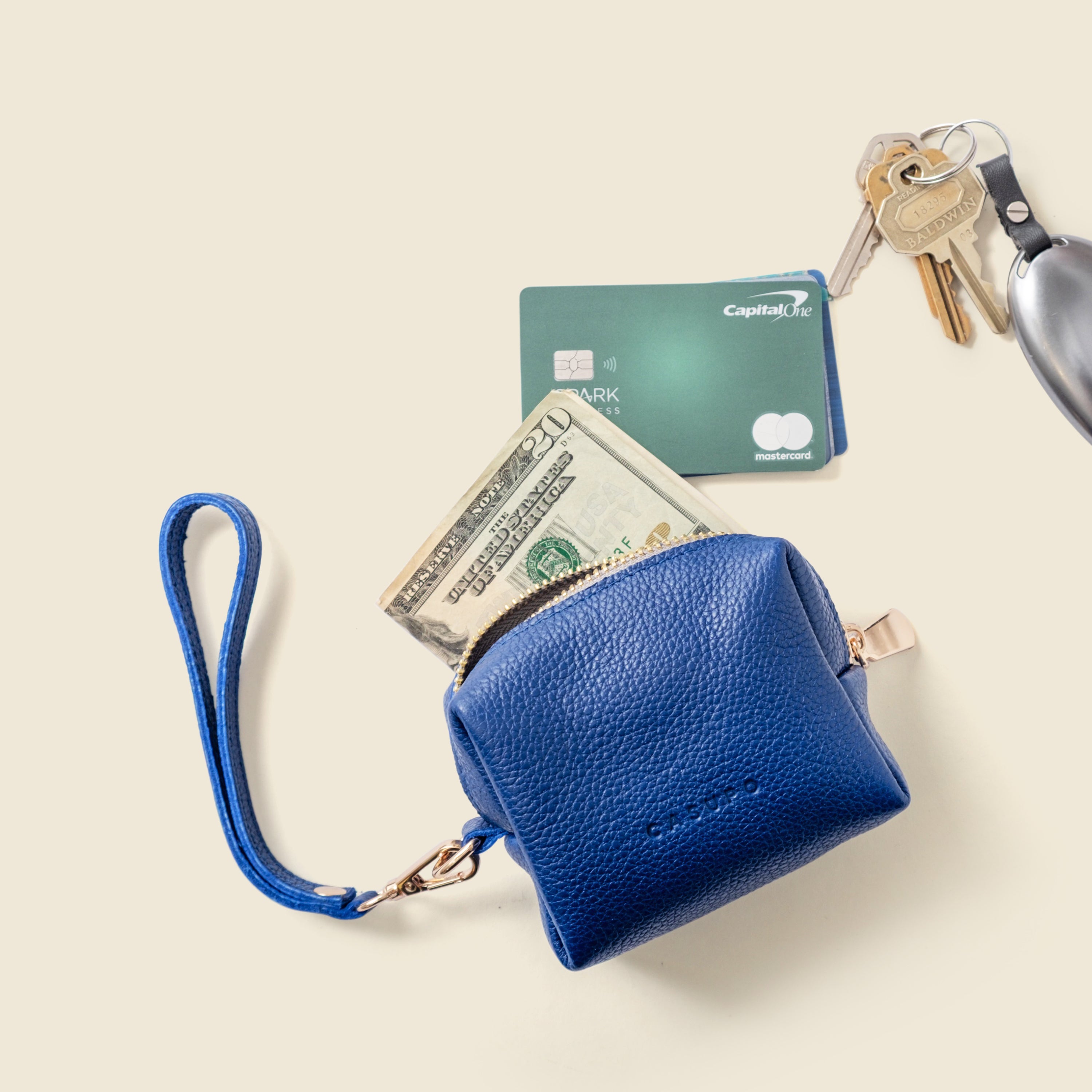 Blue leather wallet with money, card, and keys on a beige background