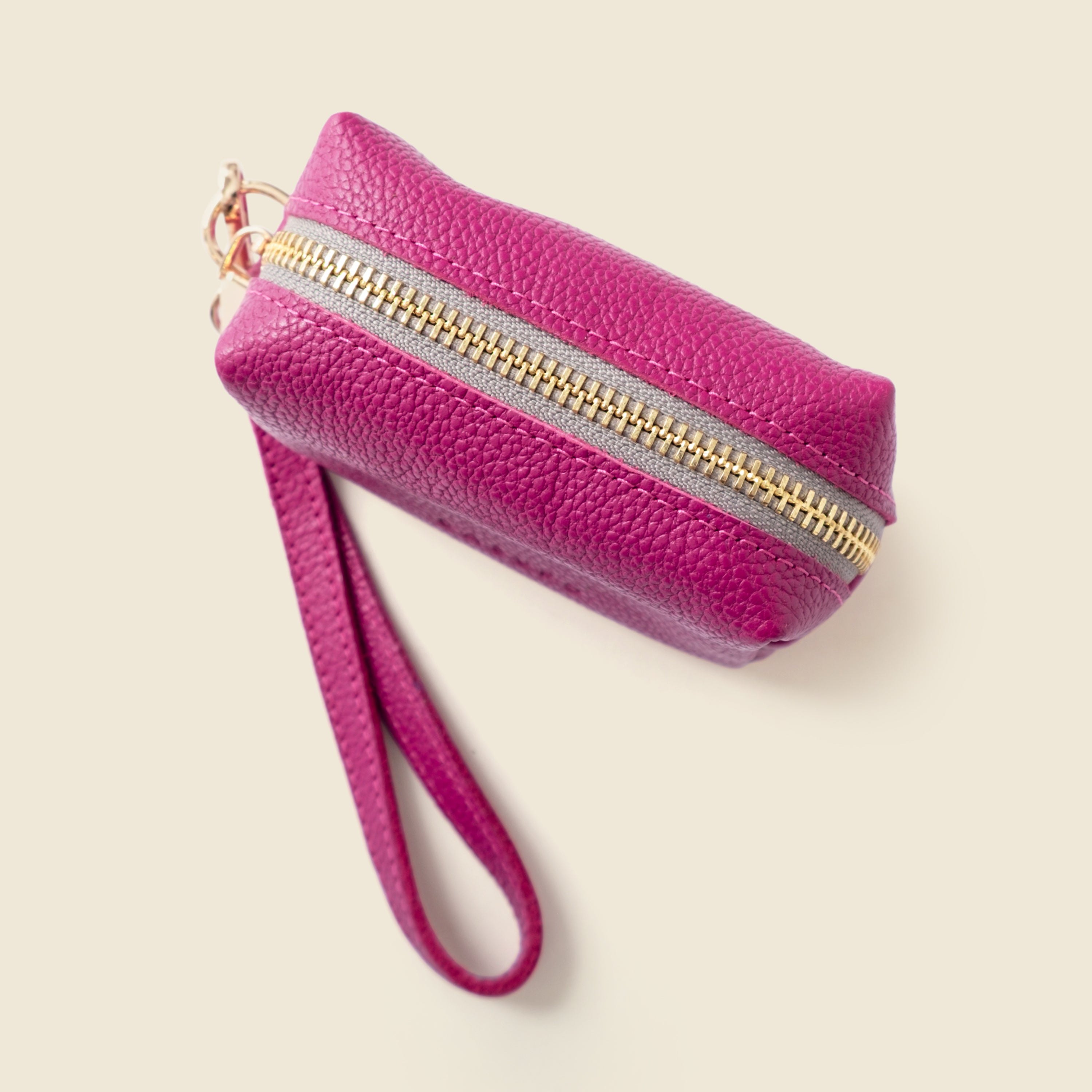 Pink wristlet with gold zipper on a beige background