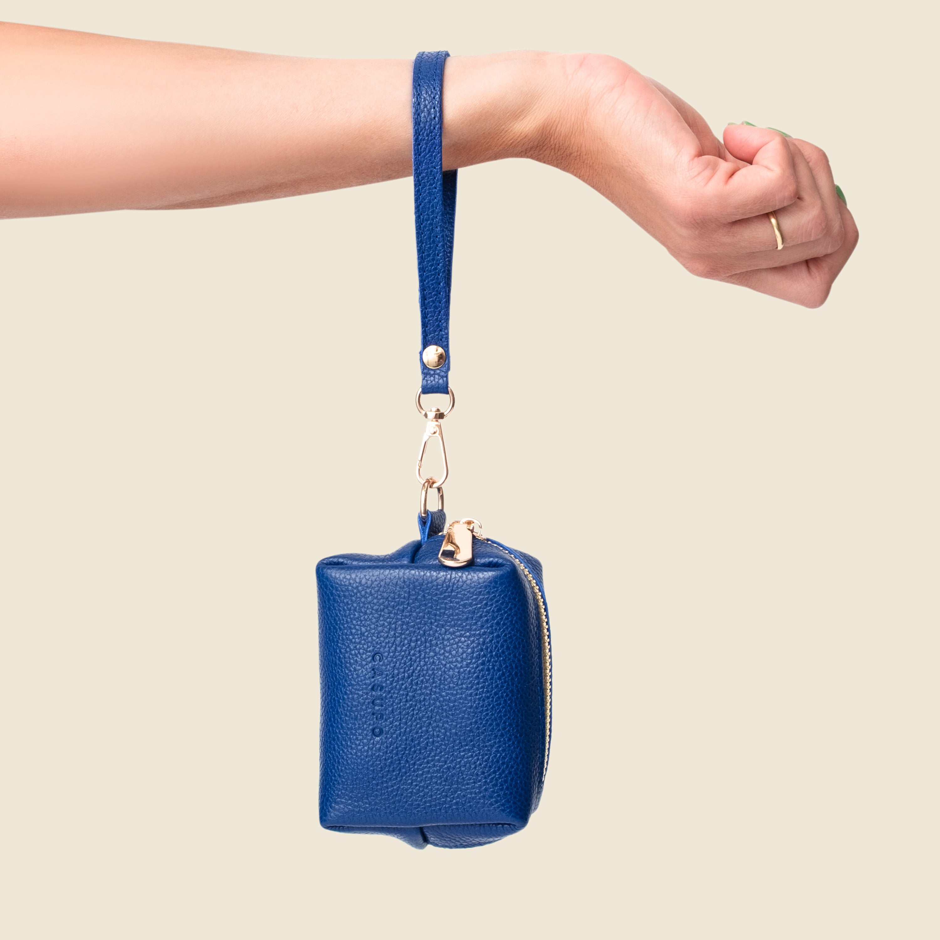 Blue leather pouch with strap held by a hand on a beige background