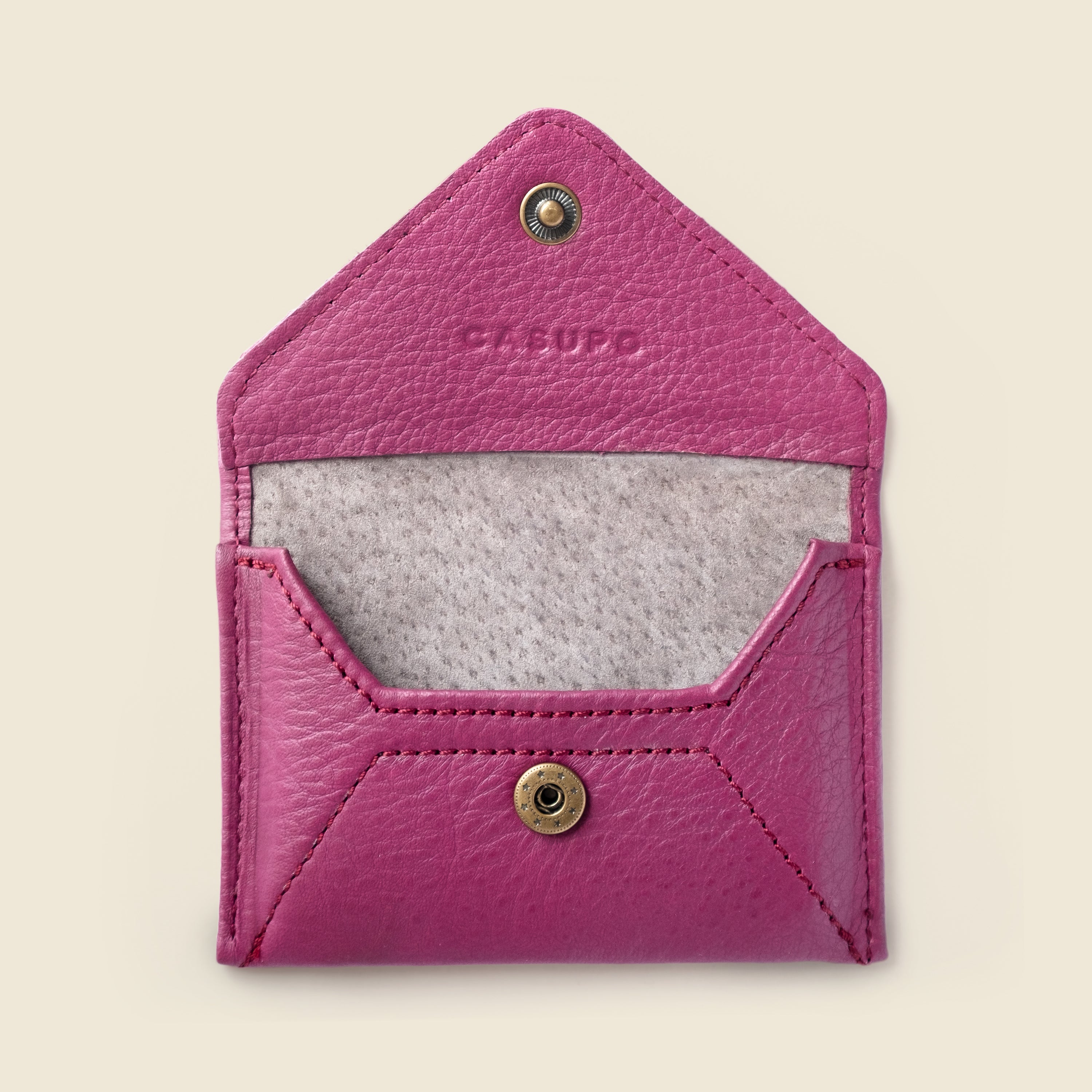 Pink leather cardholder with gold accents on a beige background