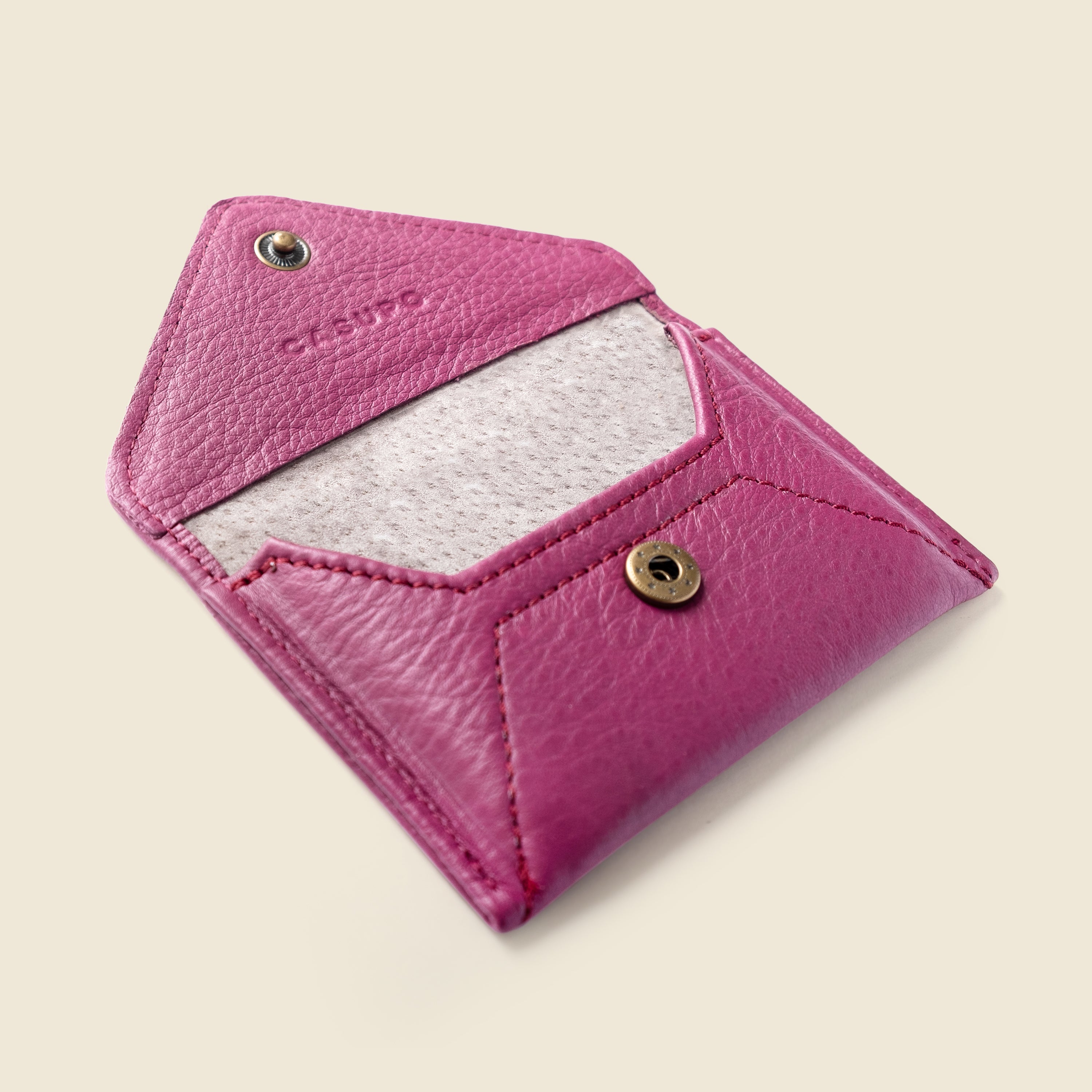 Pink leather cardholder with gold accents on a beige background