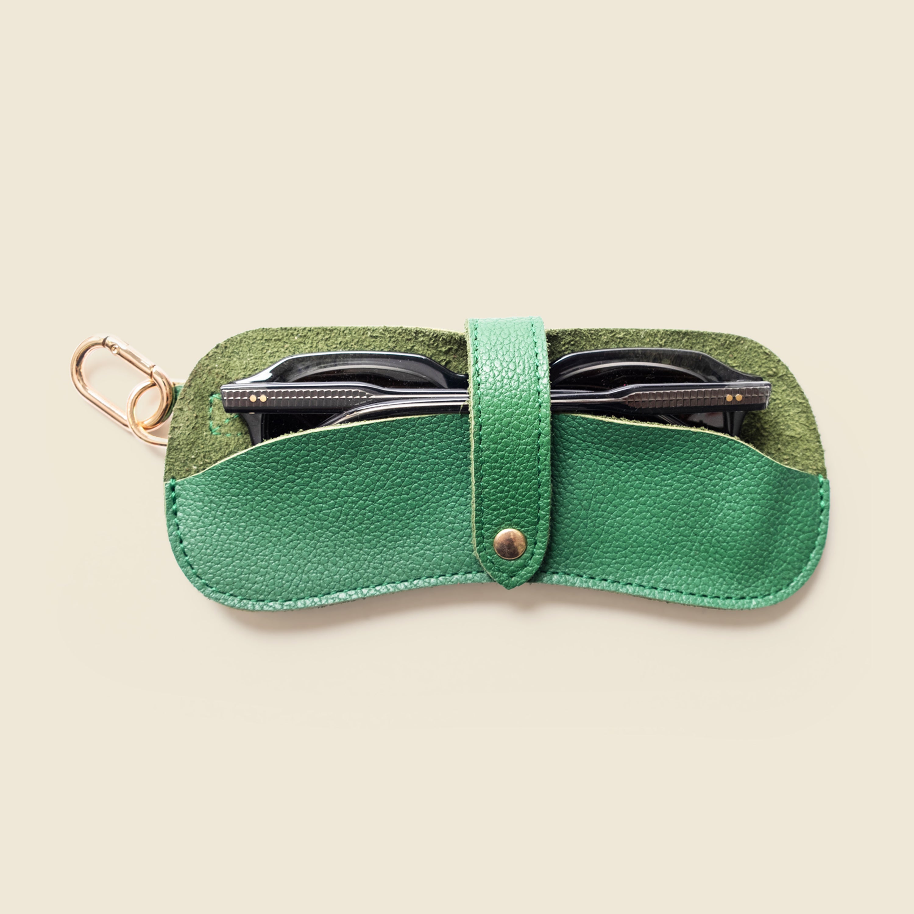 Green leather sunglasses case with a keychain on a beige background