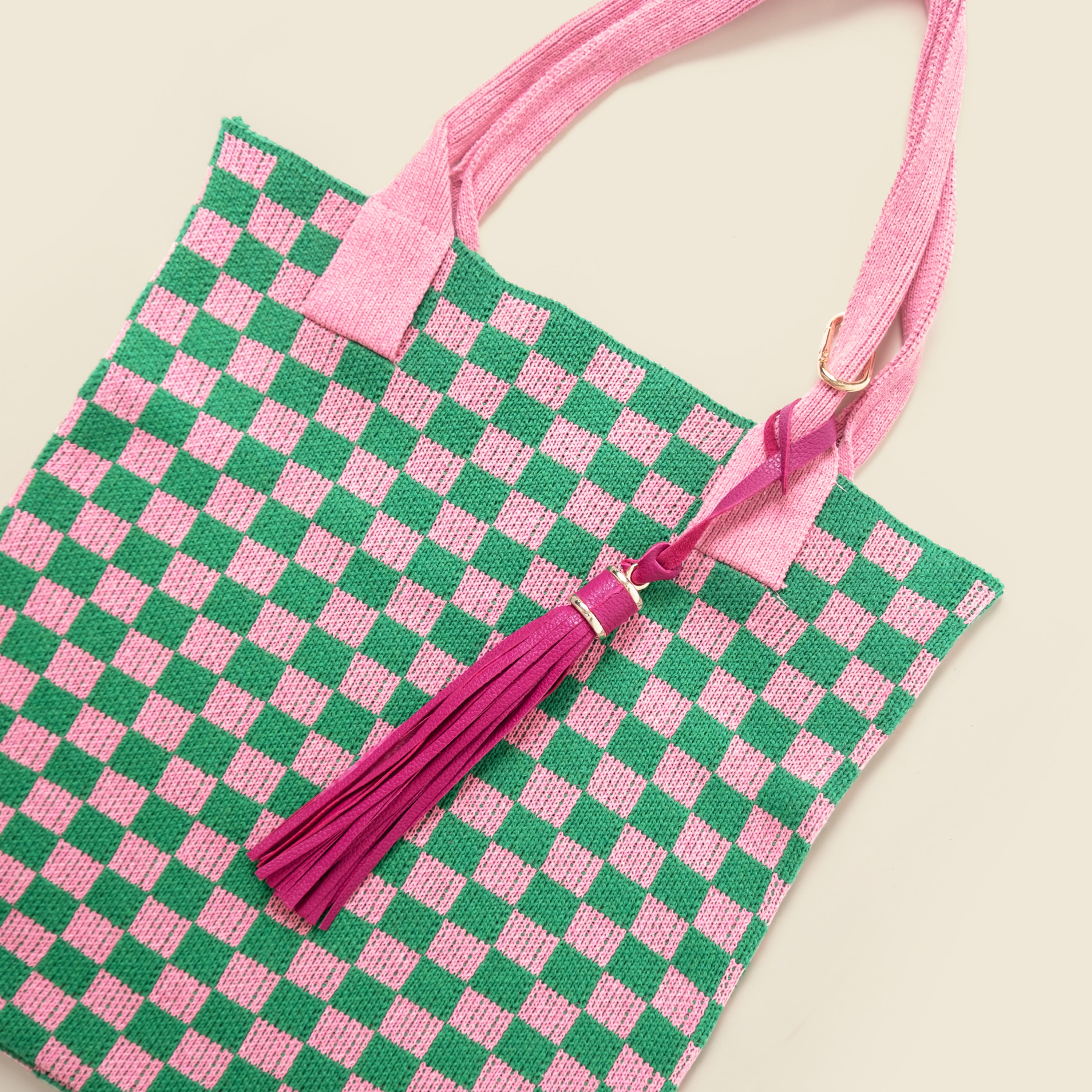 Green and pink checkered bag with a tassel on a beige background
