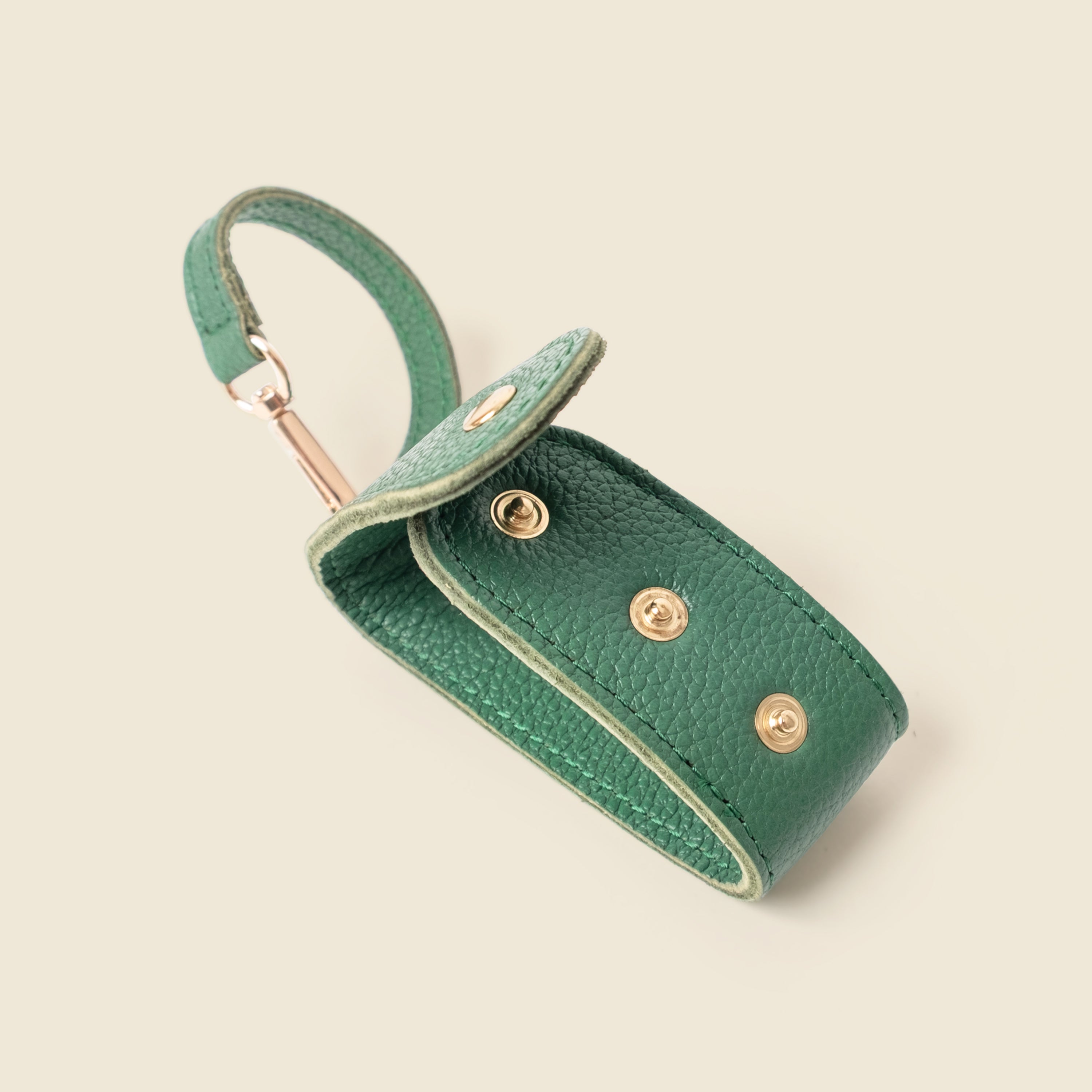 Green leather keychain pouch with gold accents on a beige background