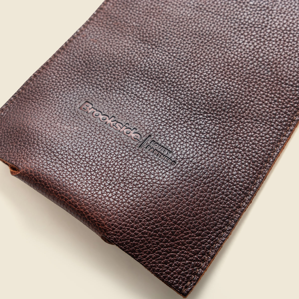 A close-up of a dark brown textured leather pouch with an embossed Brookside logo, set against a light cream background.