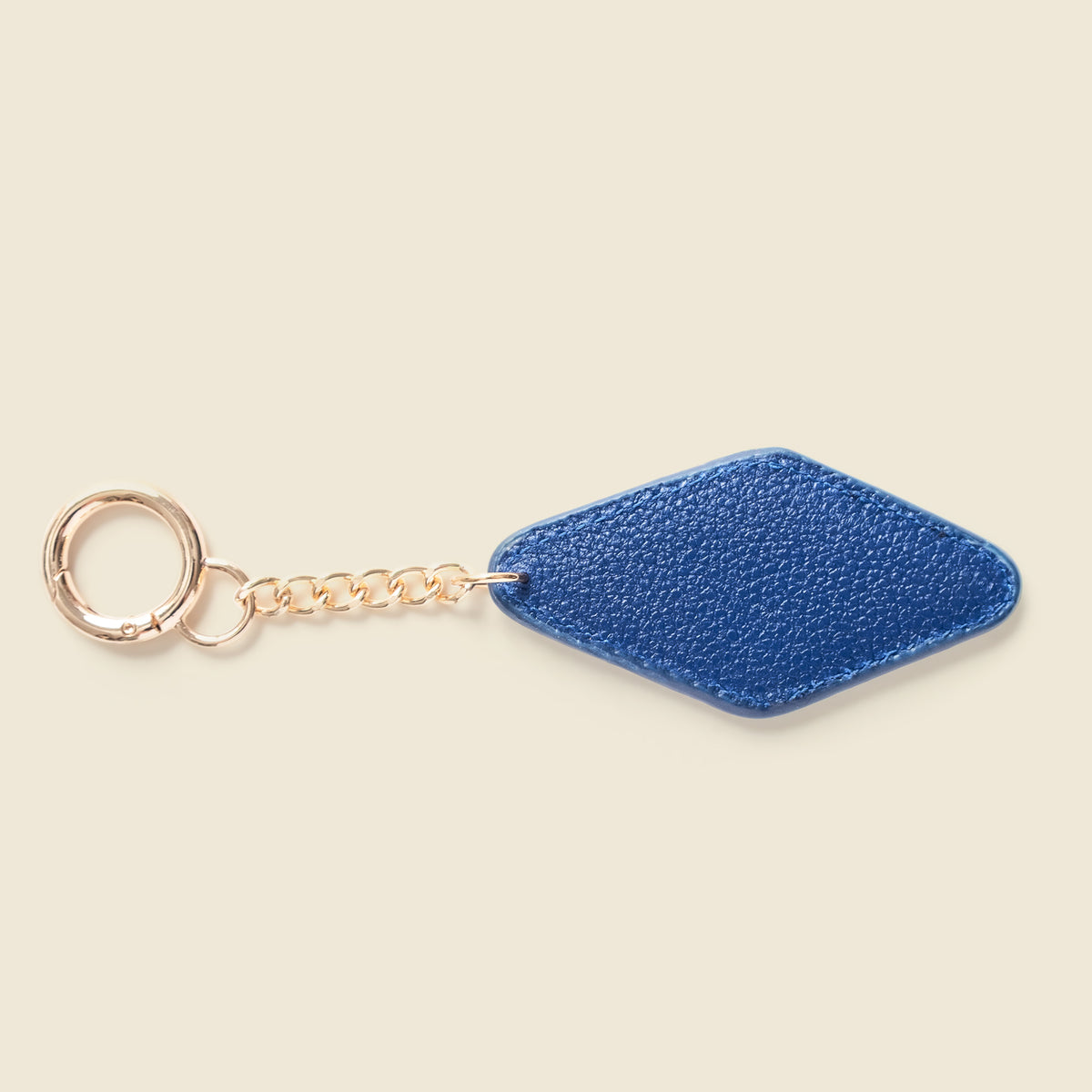 A blue textured leather keychain tag with a gold-tone chain and split ring, shown on a solid light beige background.