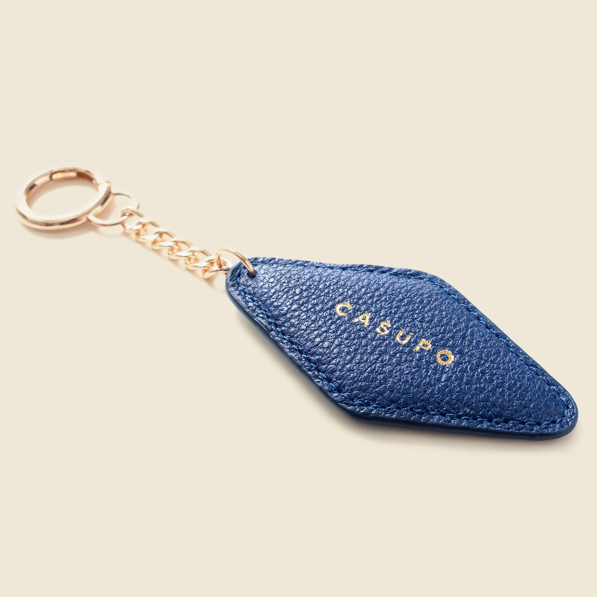 A blue textured leather keychain with a diamond-shaped tag, gold-tone chain, and a gold logo reading 'CASUPO' on a light beige background.