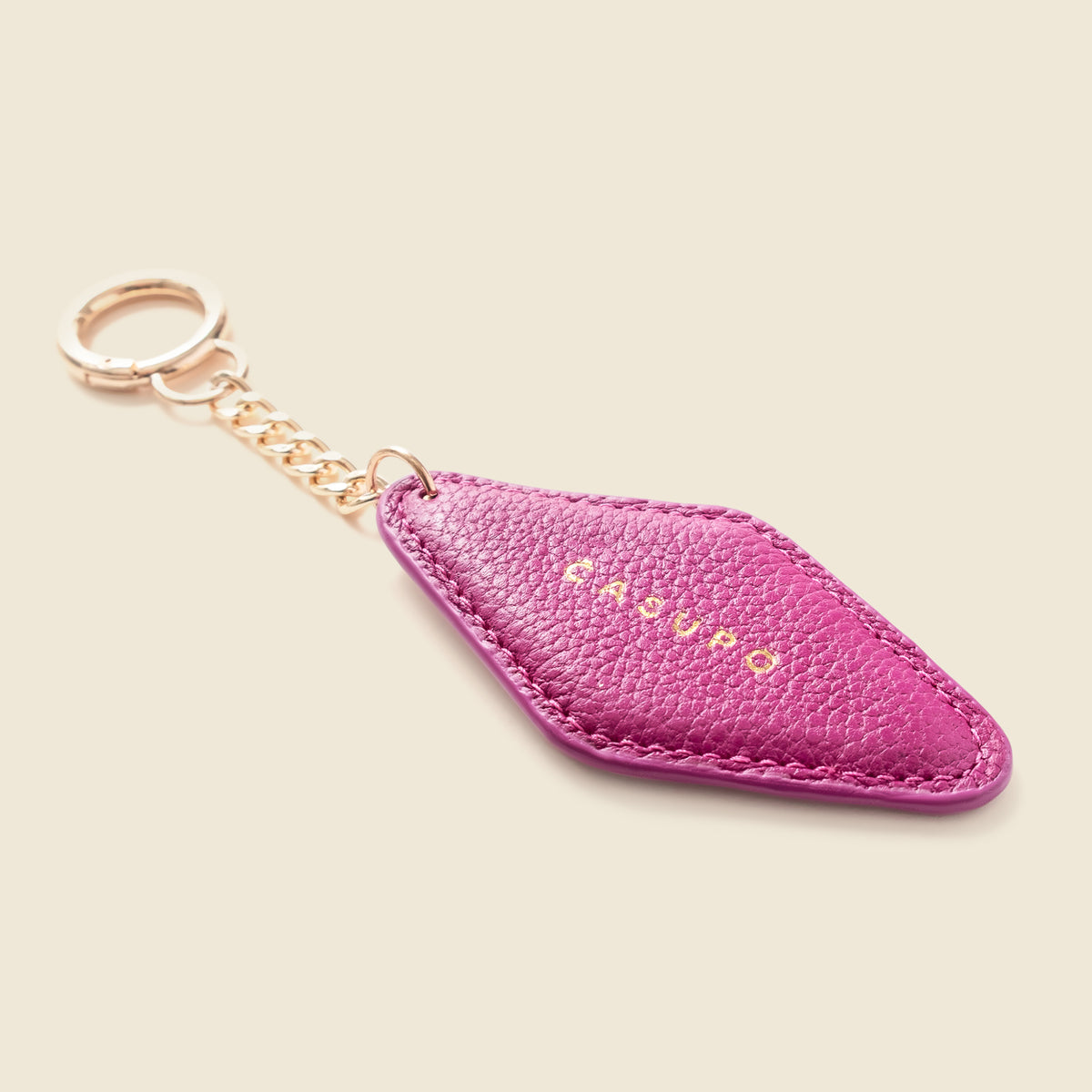 A pink textured leather keychain with a gold-tone chain and key ring, featuring the brand name 'CASASPO' in gold lettering on the front, set against a solid light beige background.
