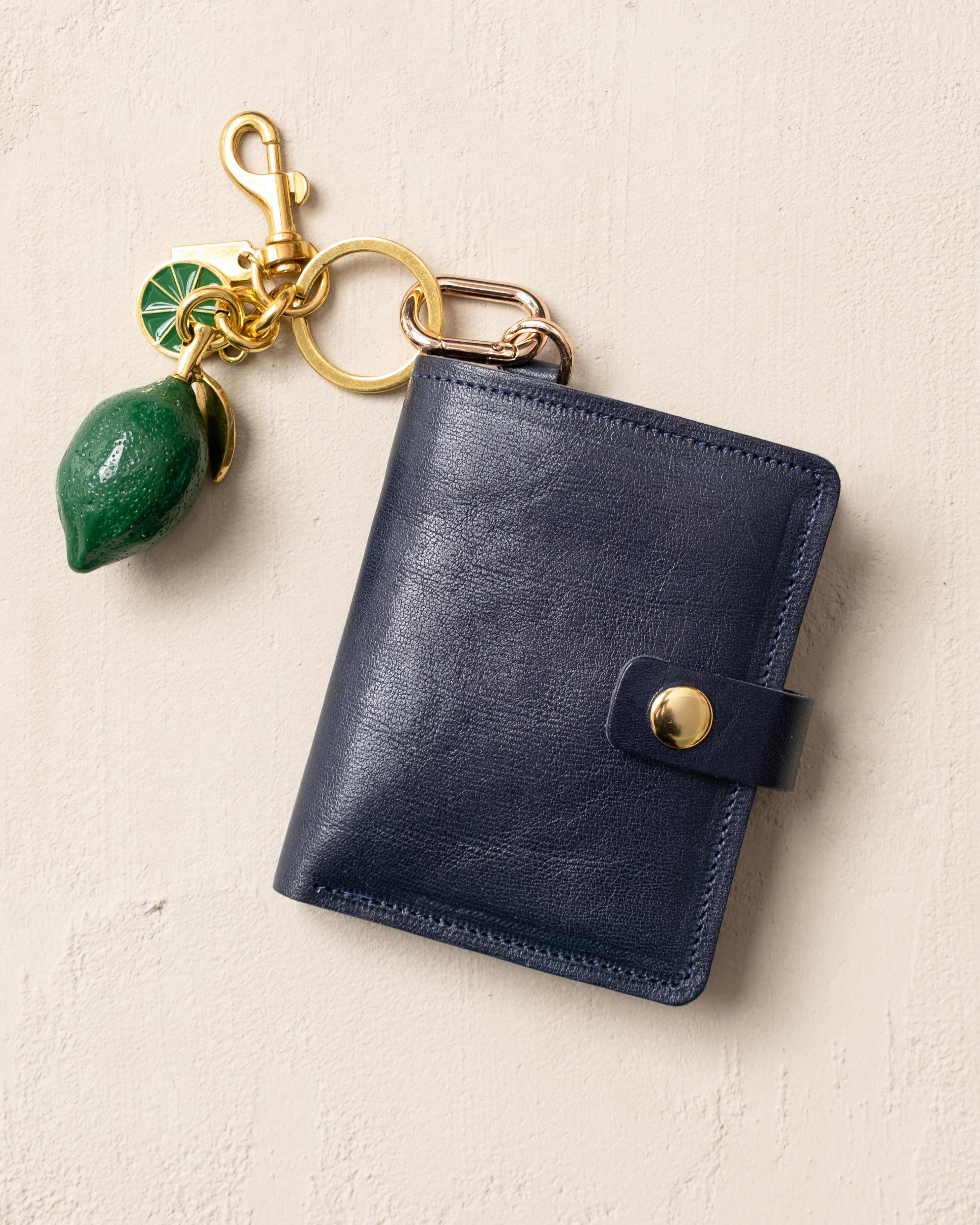 Blue leather wallet with gold clasp and green charm on a beige background