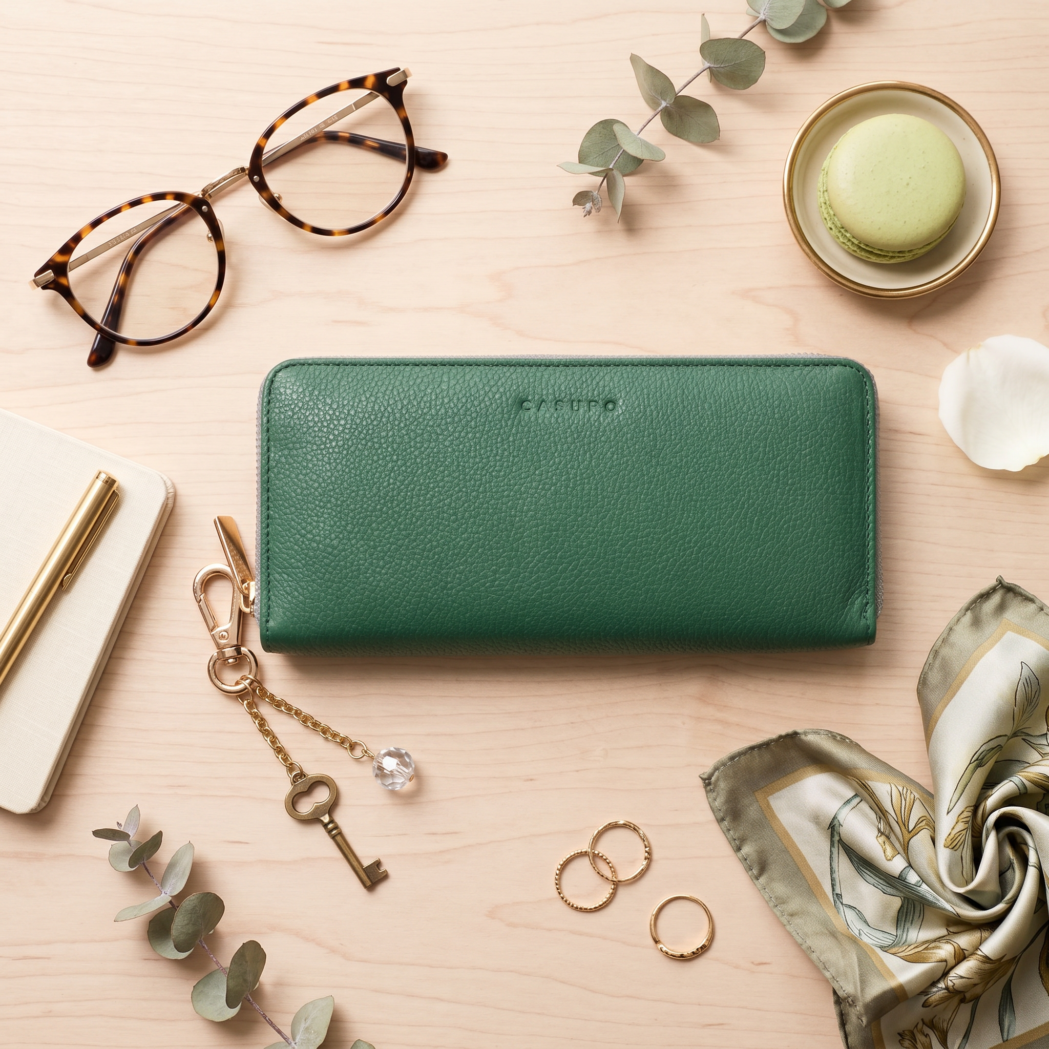 Green wallet on a wooden surface with glasses, macaron, and keychain.