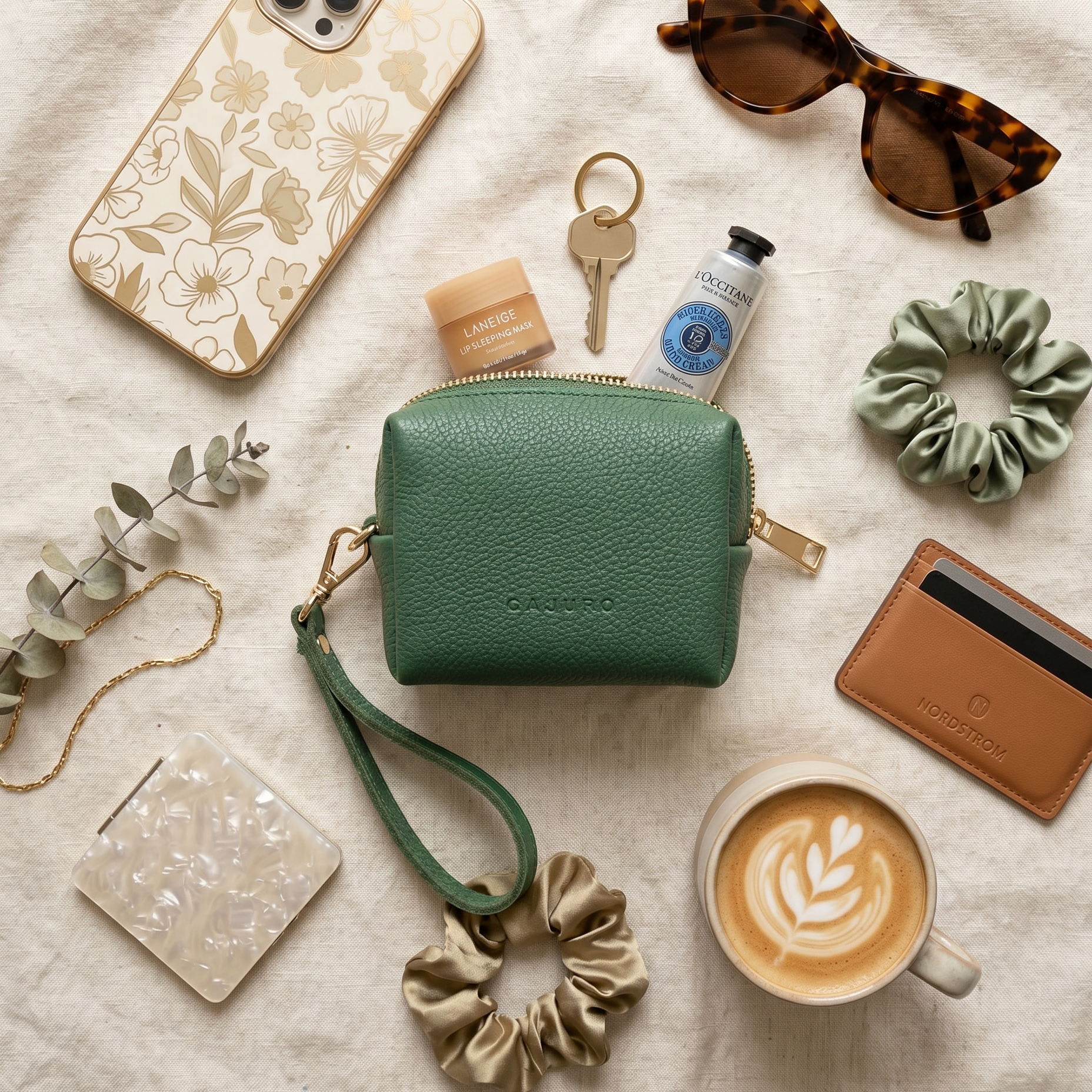 Green clutch bag with various items including a phone, scrunchies, and a coffee cup on a light surface.