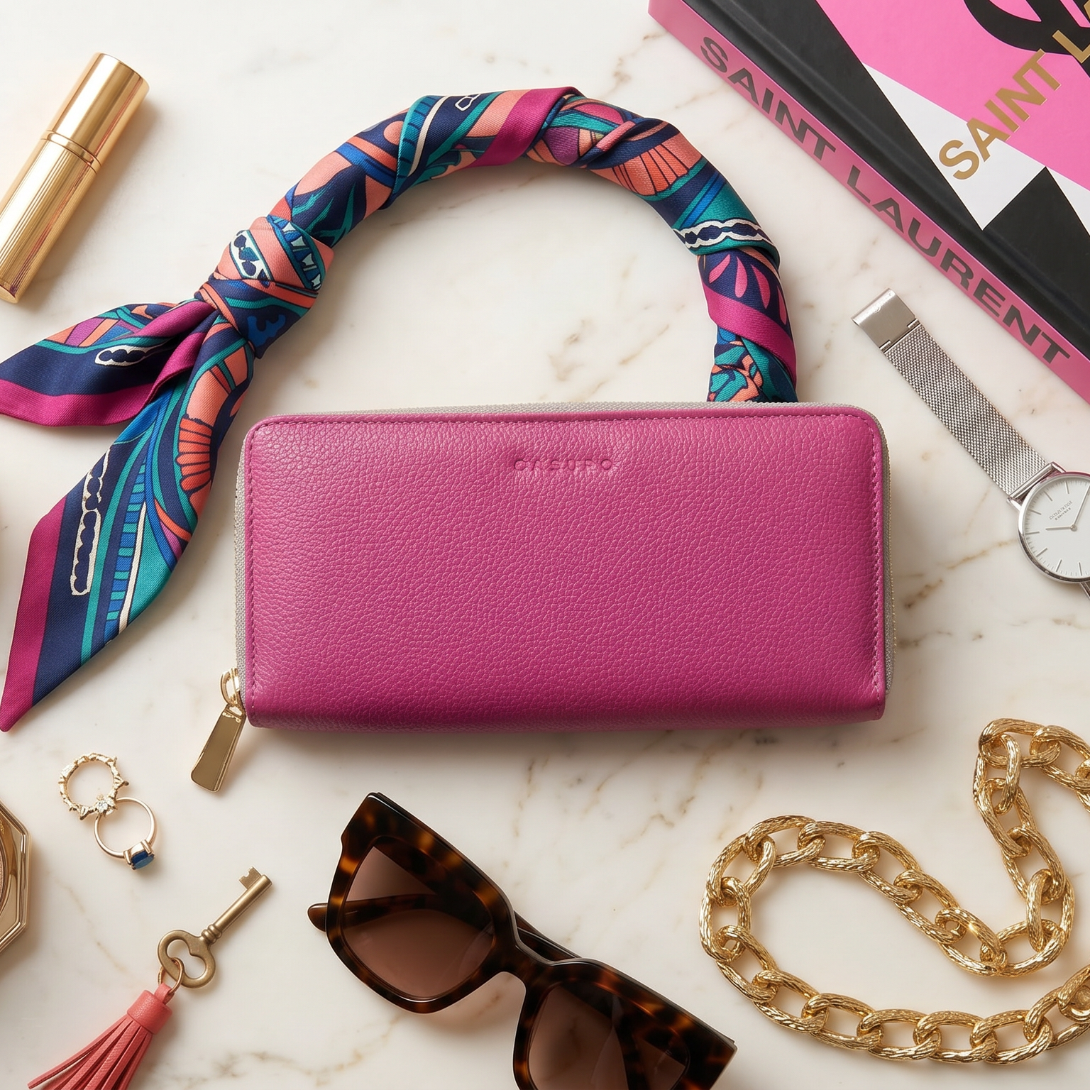 Pink wallet with colorful scarf, YSL box, sunglasses, and other accessories on a marble surface