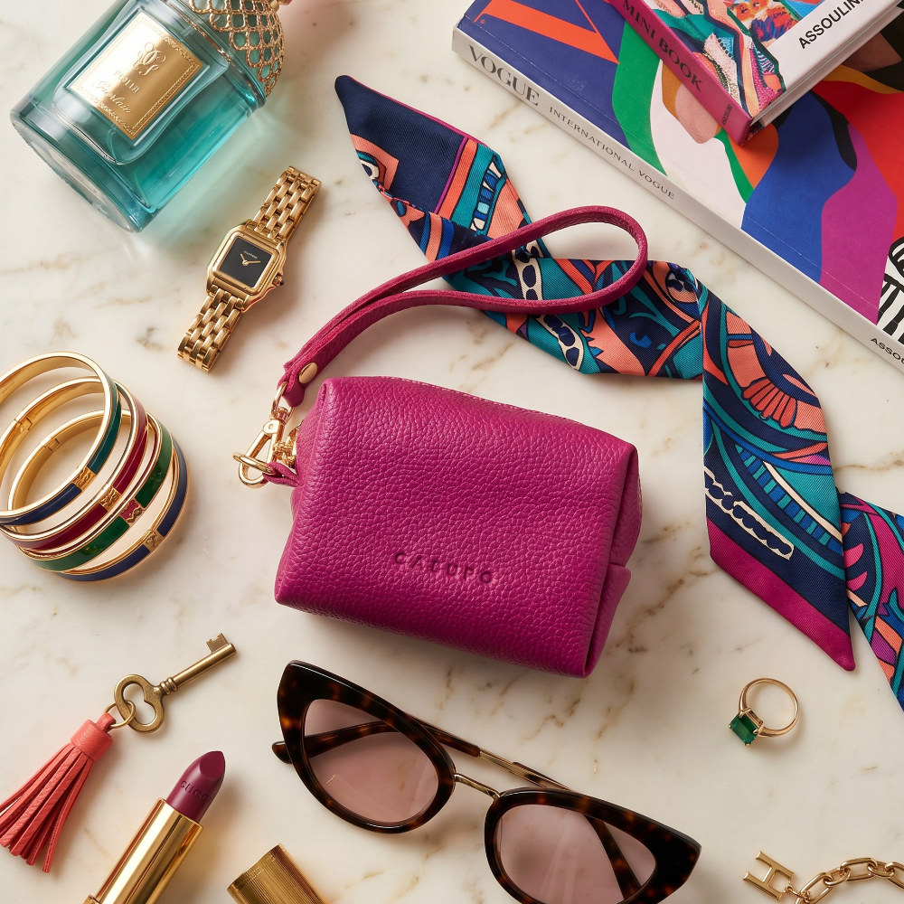 Collection of fashion items including a pink wallet, sunglasses, lipstick, and jewelry on a marble surface.
