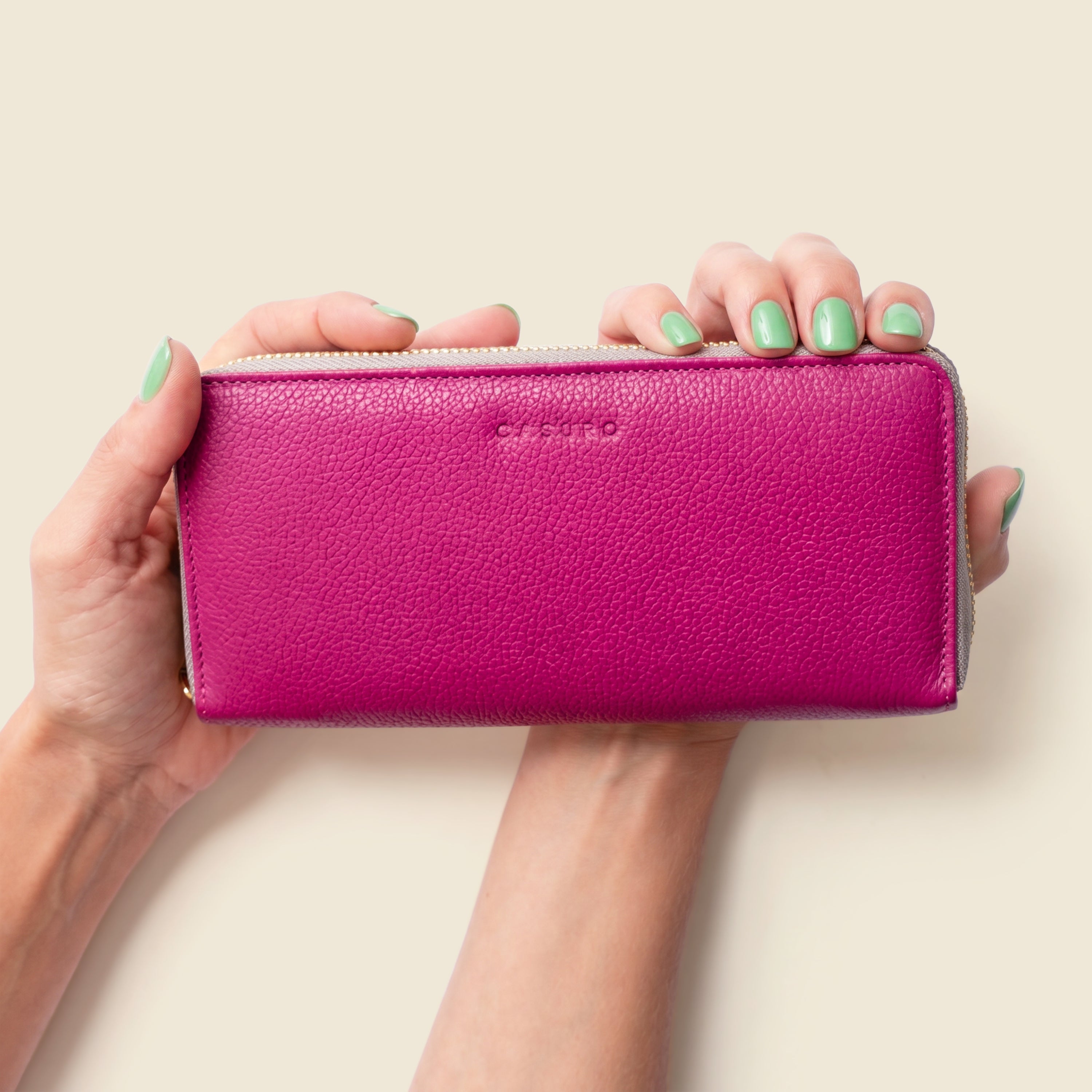 Pink wallet held by hands with green nail polish on a beige background