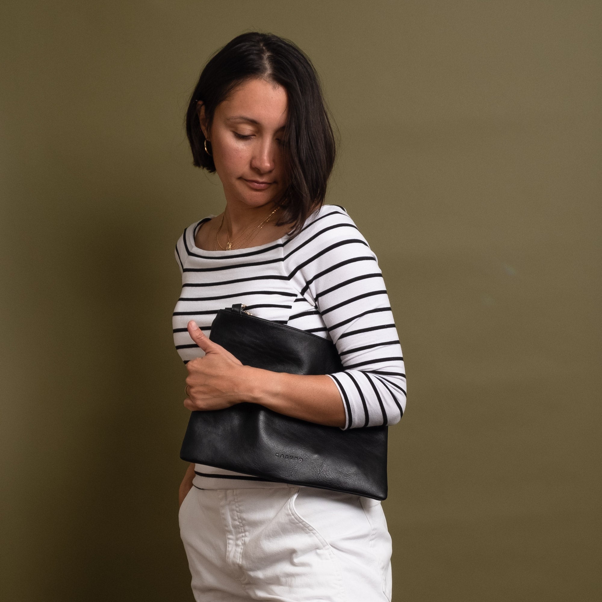 Woman wearing black leather clutch under her arm. She is wearing a white and black striped top and white jeans