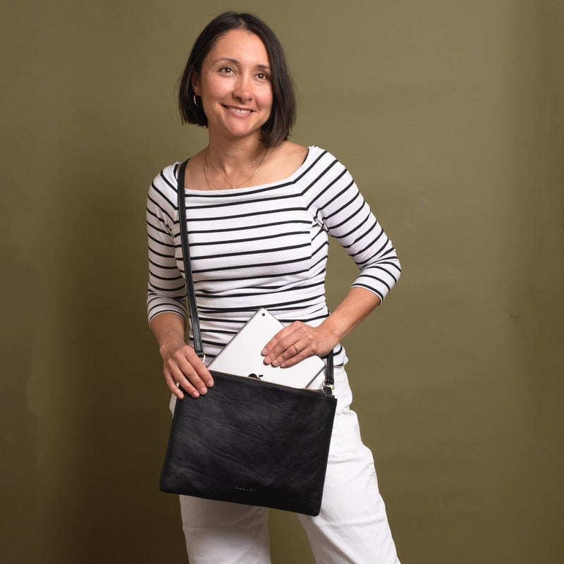 Woman putting ipad inside a black leather crossbody bag