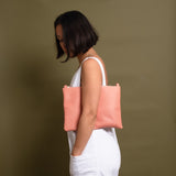 woman wearing coral pink leather crossbody bag under her arm.