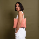 woman wearing salmon pink leather crossbody bag under her arm as a clutch