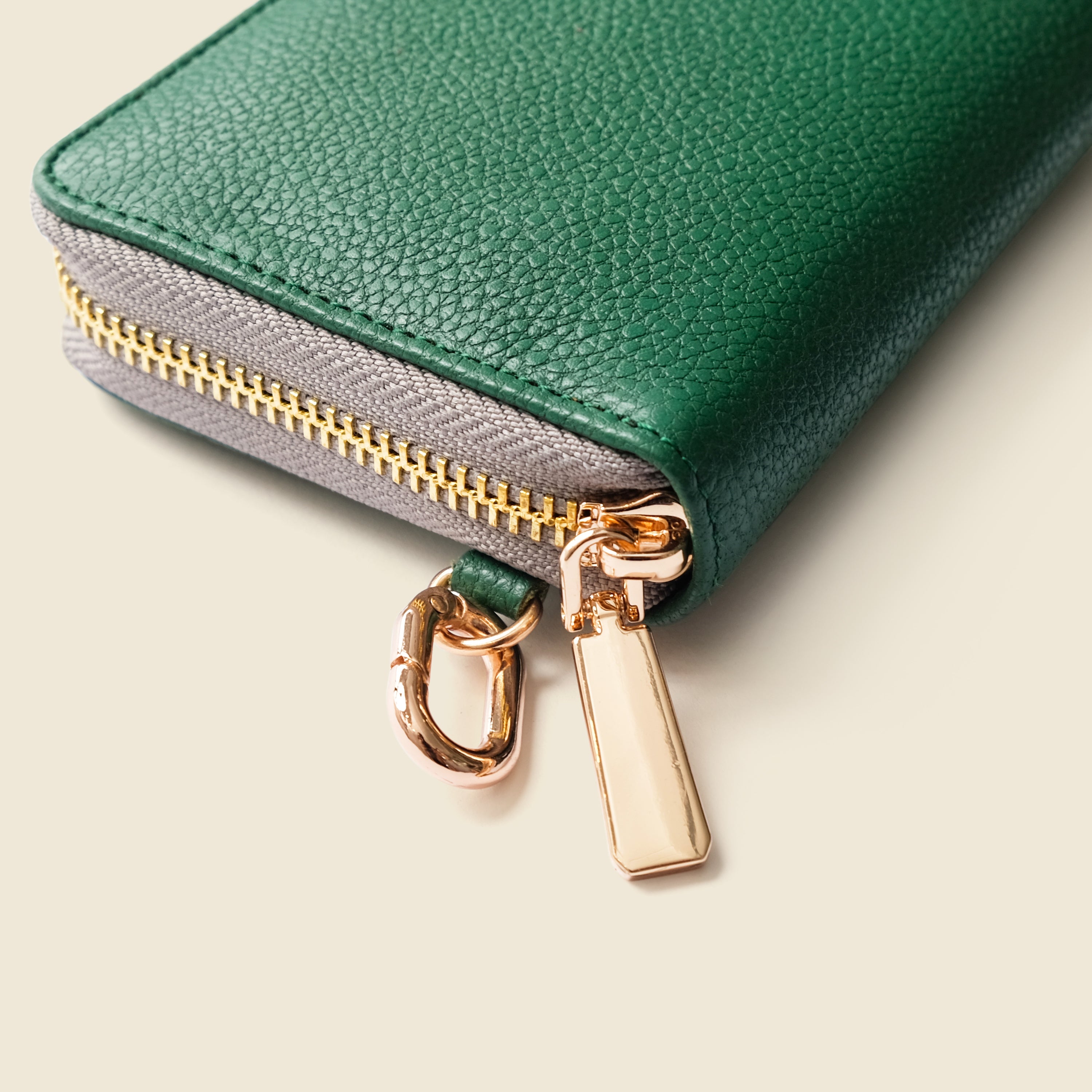 Green leather wallet with gold zipper pull on a beige background