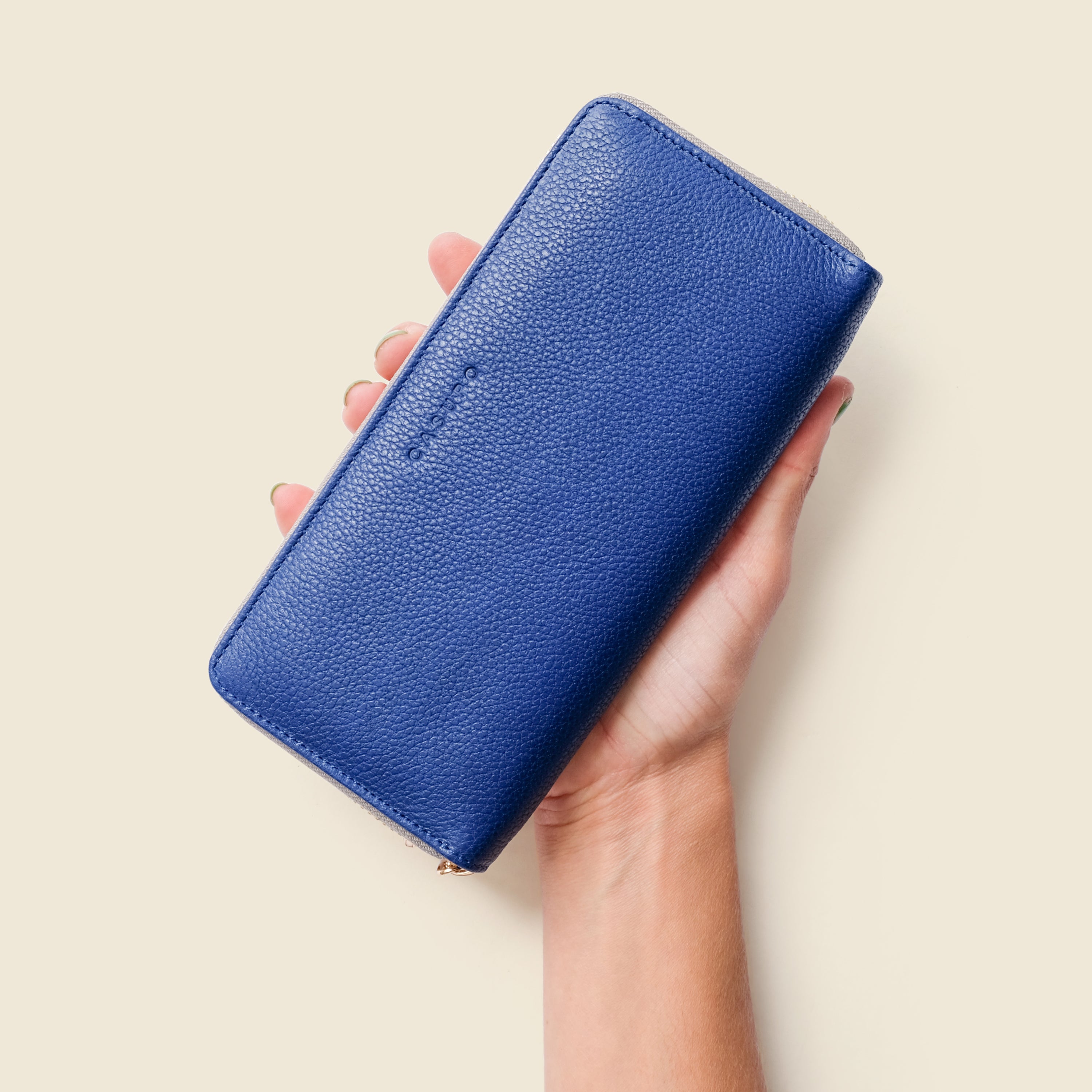 Hand holding a blue wallet against a beige background