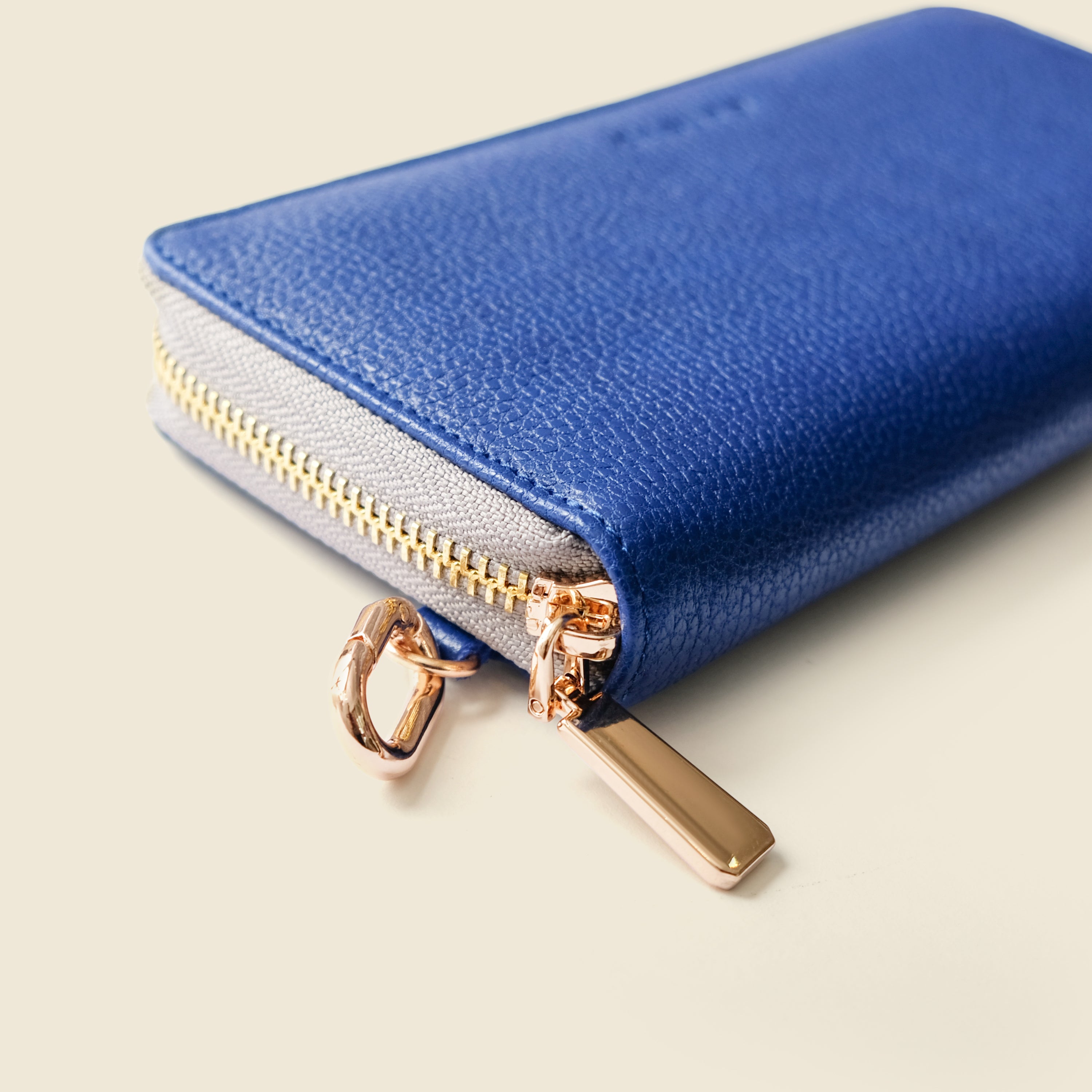 Blue wallet with gold zipper and clasp on a beige background