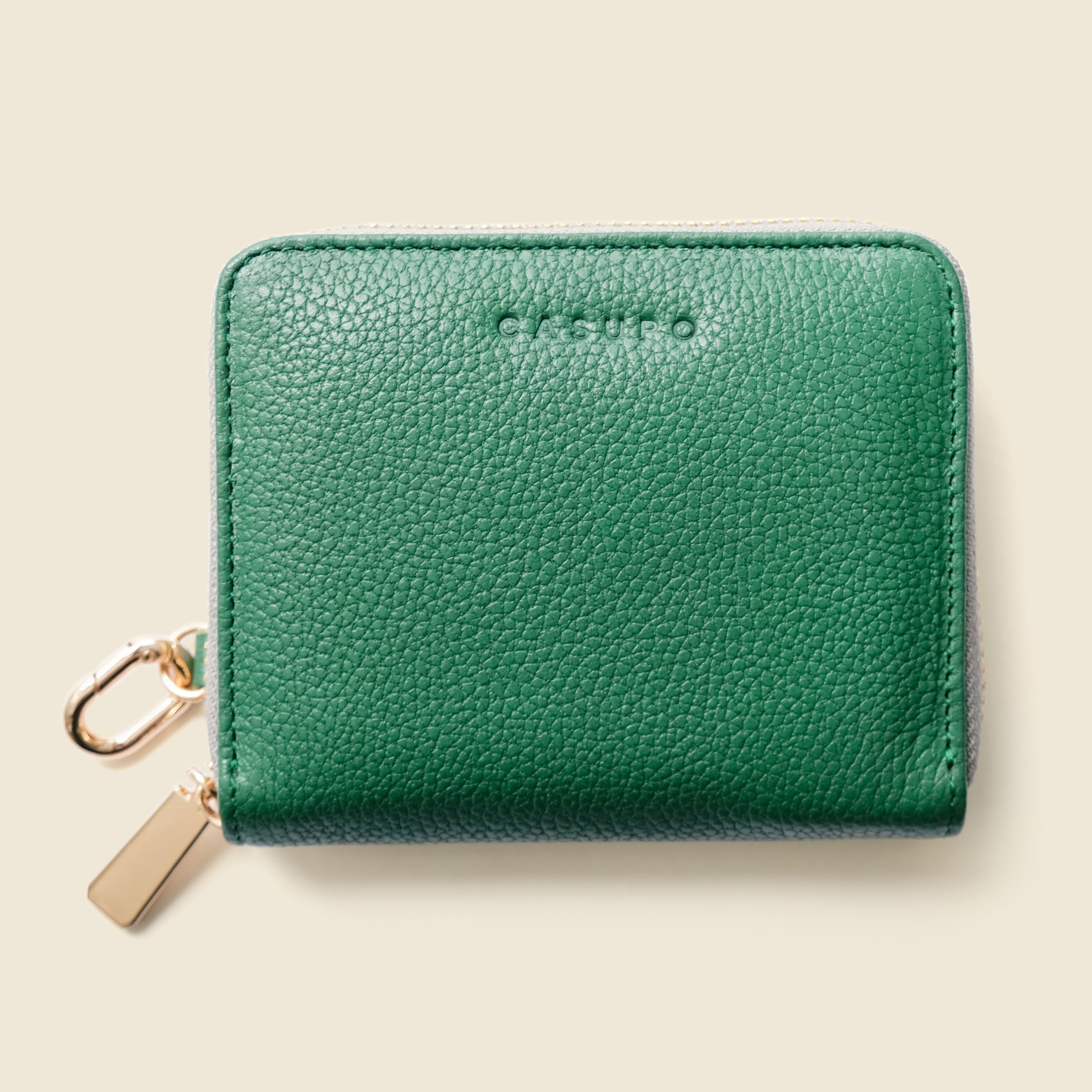 Green leather wallet with gold zipper on a beige background