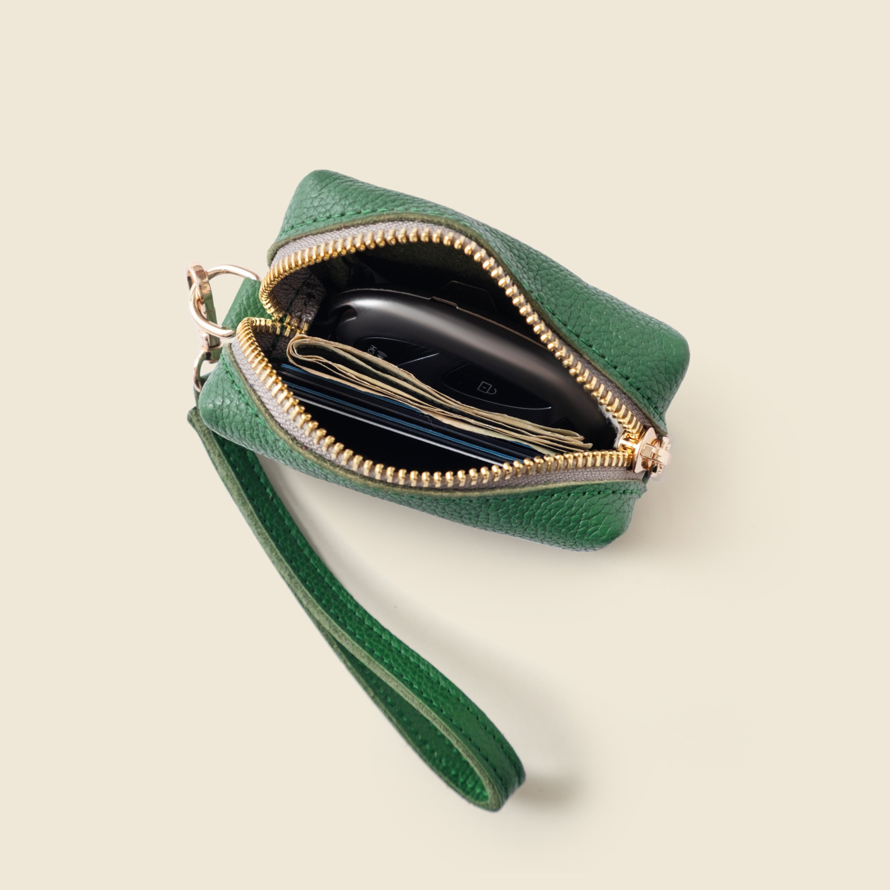 Green pouch with gold zipper on a beige background