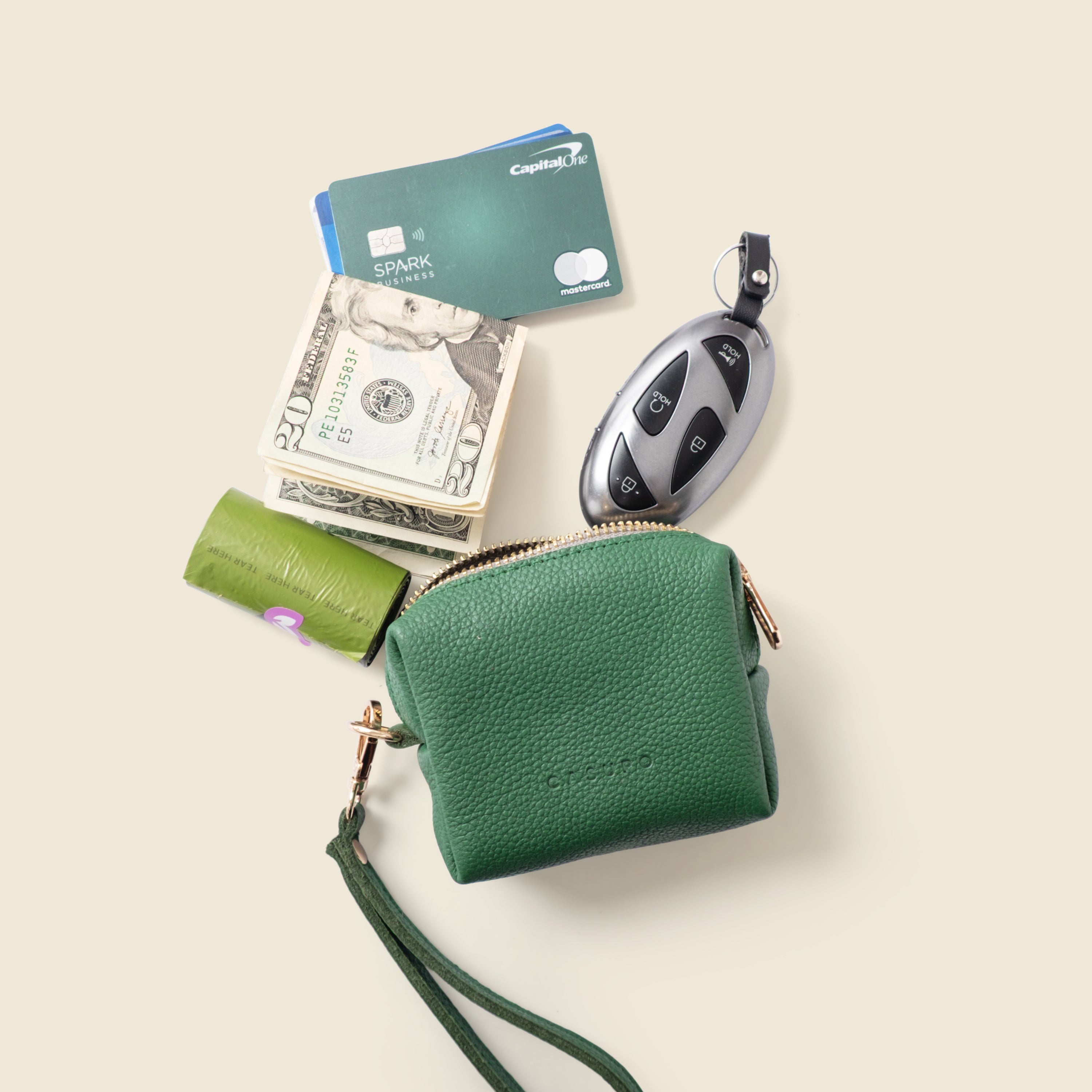 Green leather wallet with money, cards, and car keys on a beige background