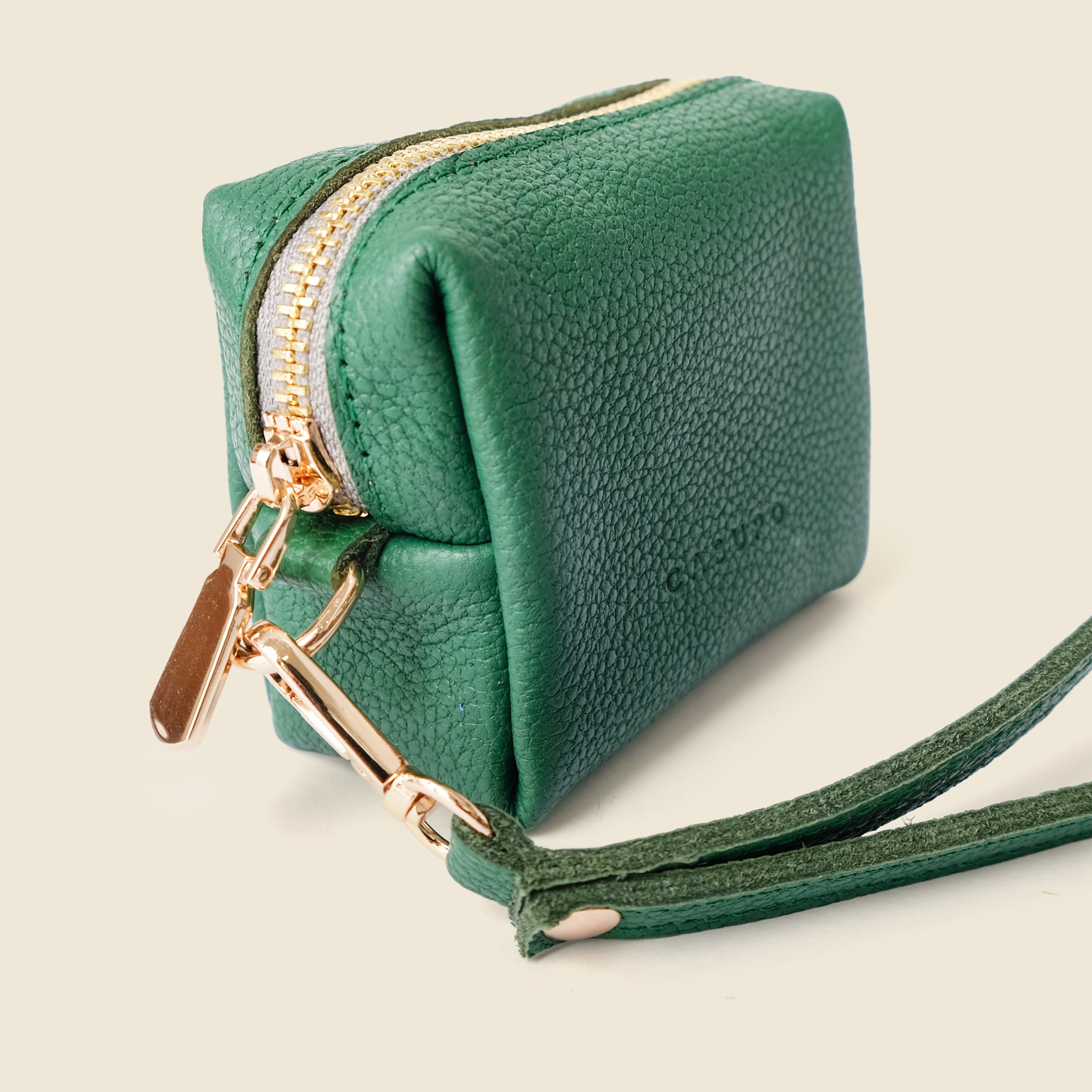 Green leather clutch with gold zipper and strap on a beige background