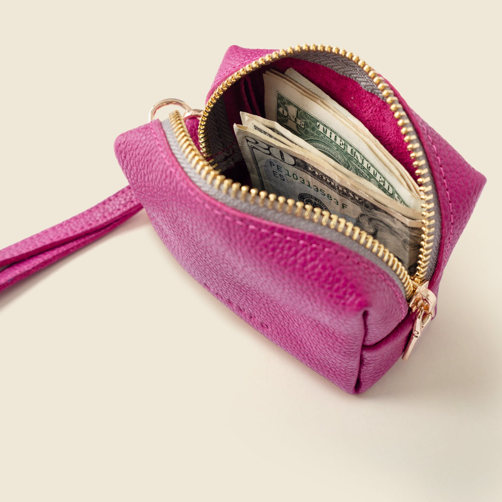 Pink purse with gold zipper open, revealing money on a light beige background