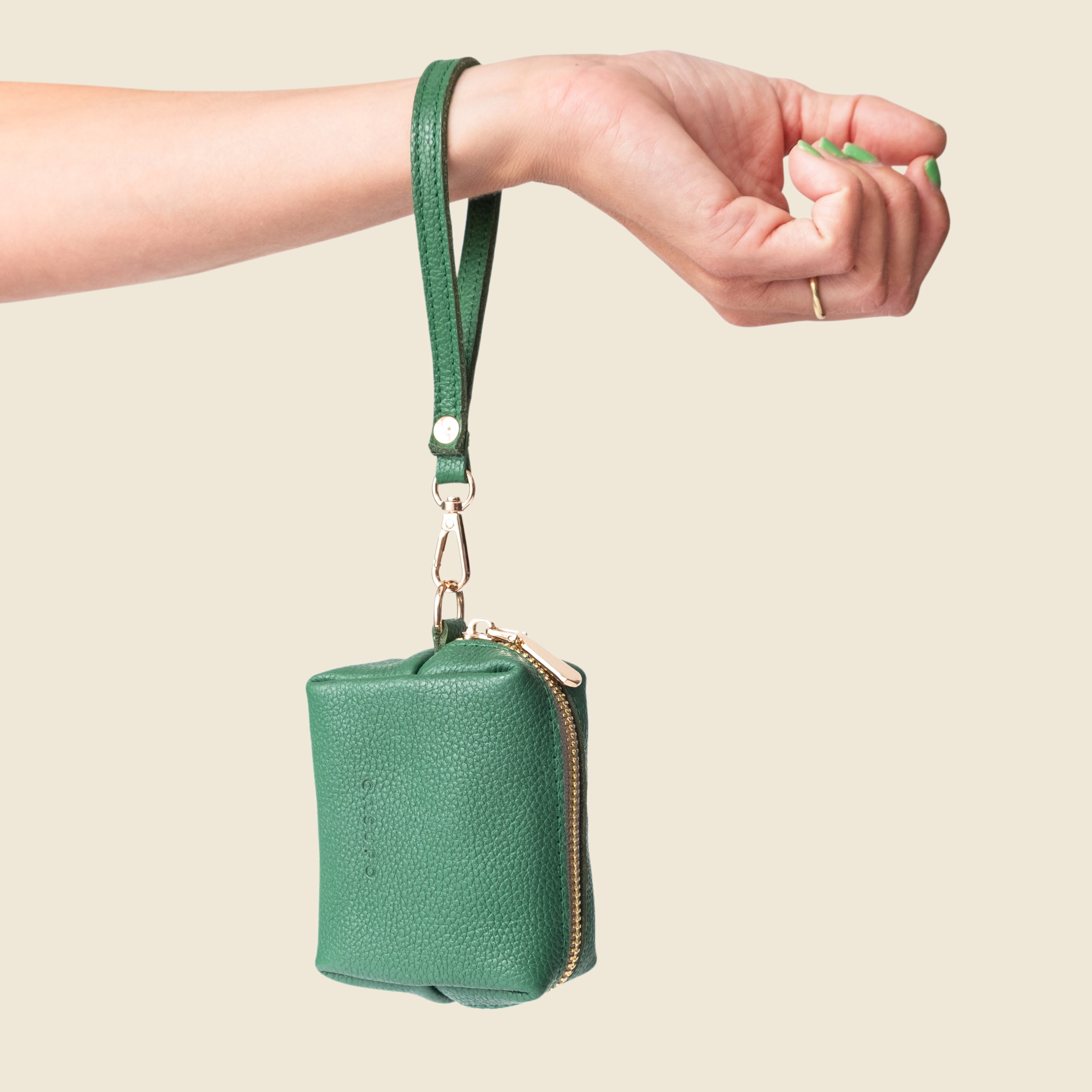 Green leather pouch with wrist strap held by a hand against a beige background