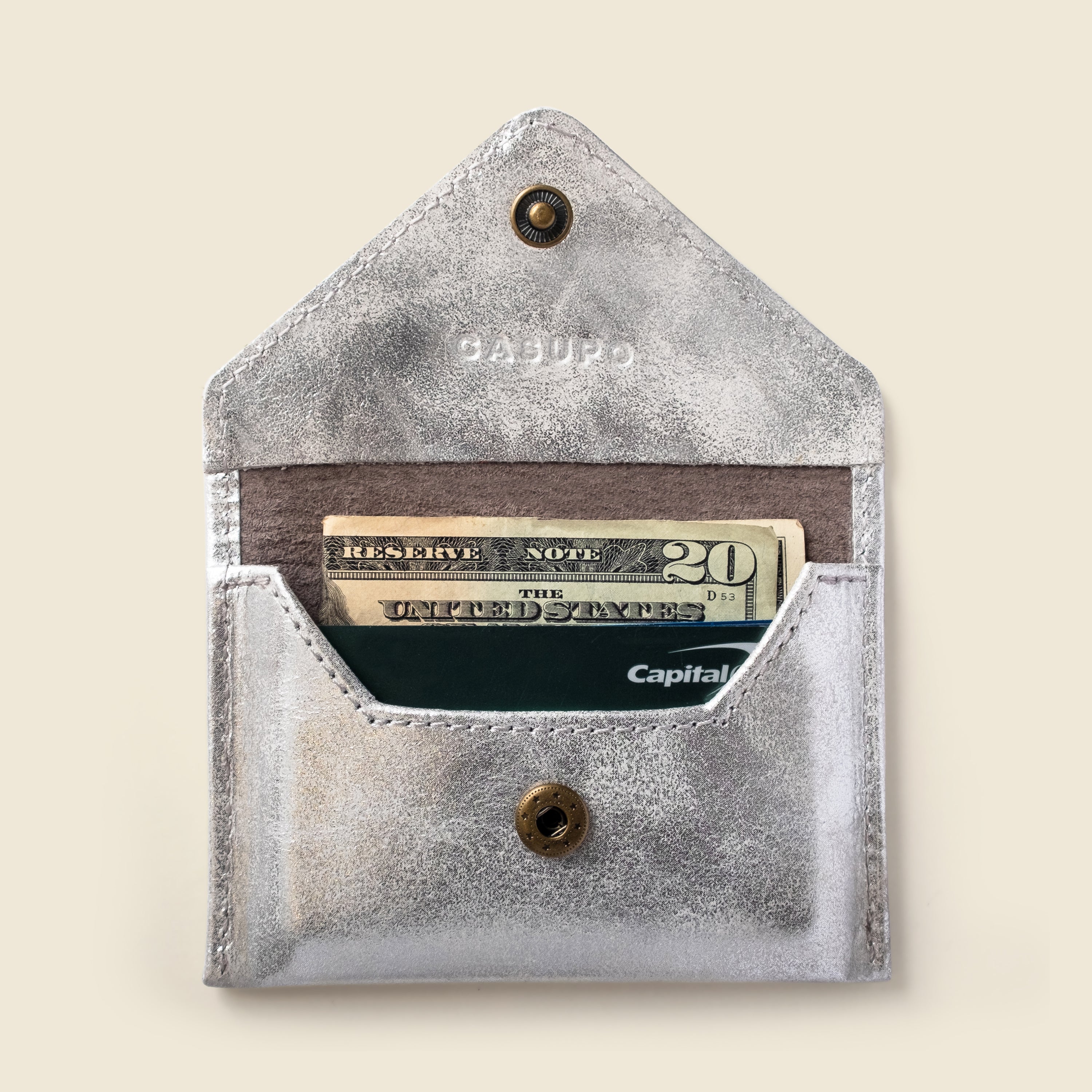 Silver leather wallet with currency and card inside on a beige background