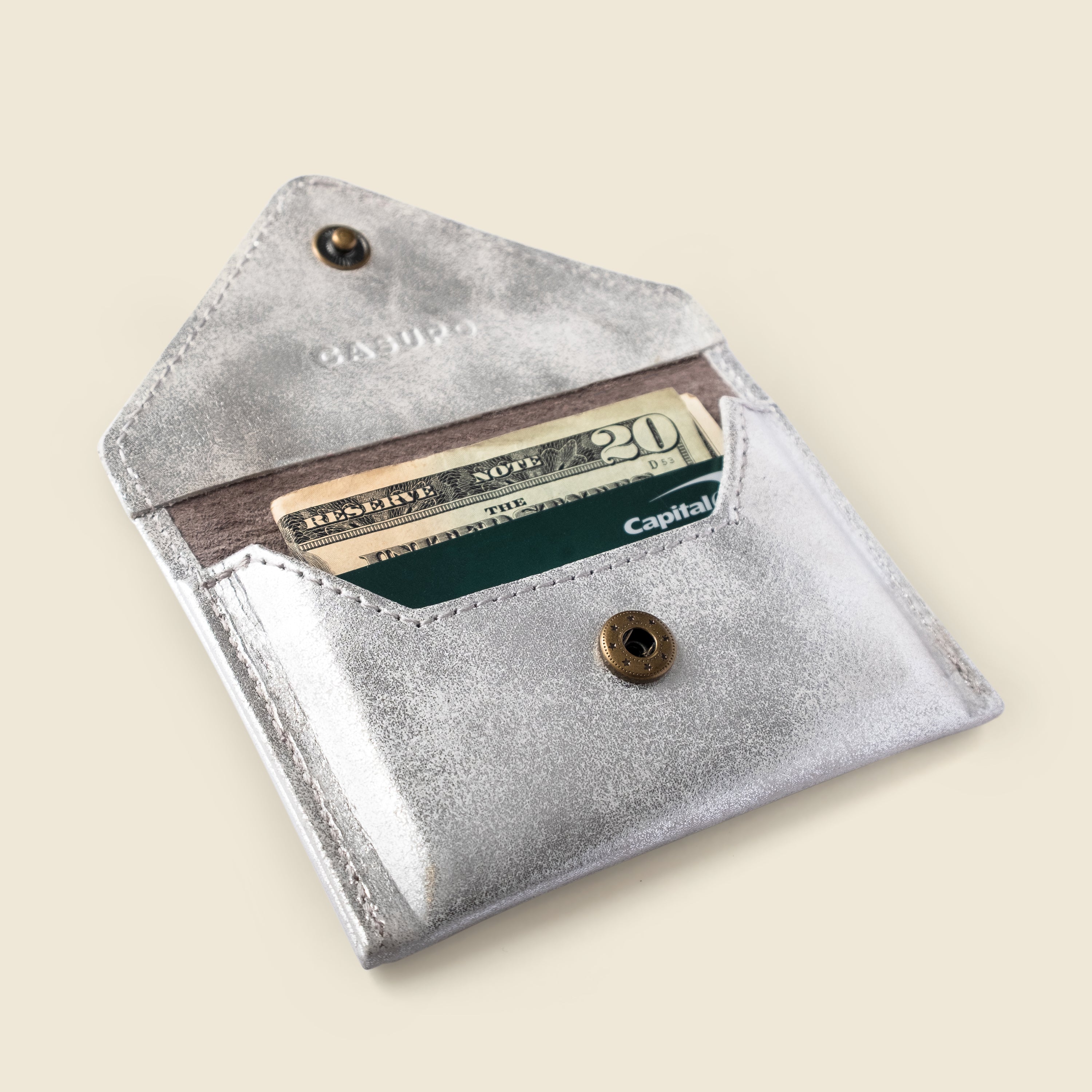 Silver wallet with a card and cash inside on a beige background