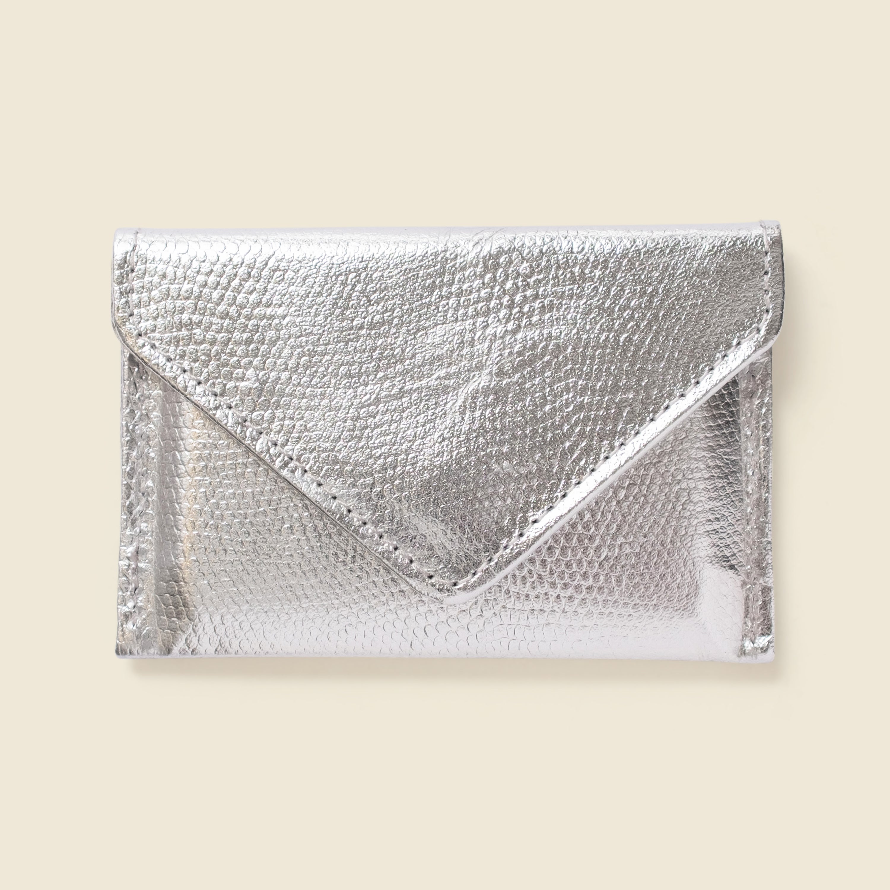 Silver clutch bag with textured surface on a beige background