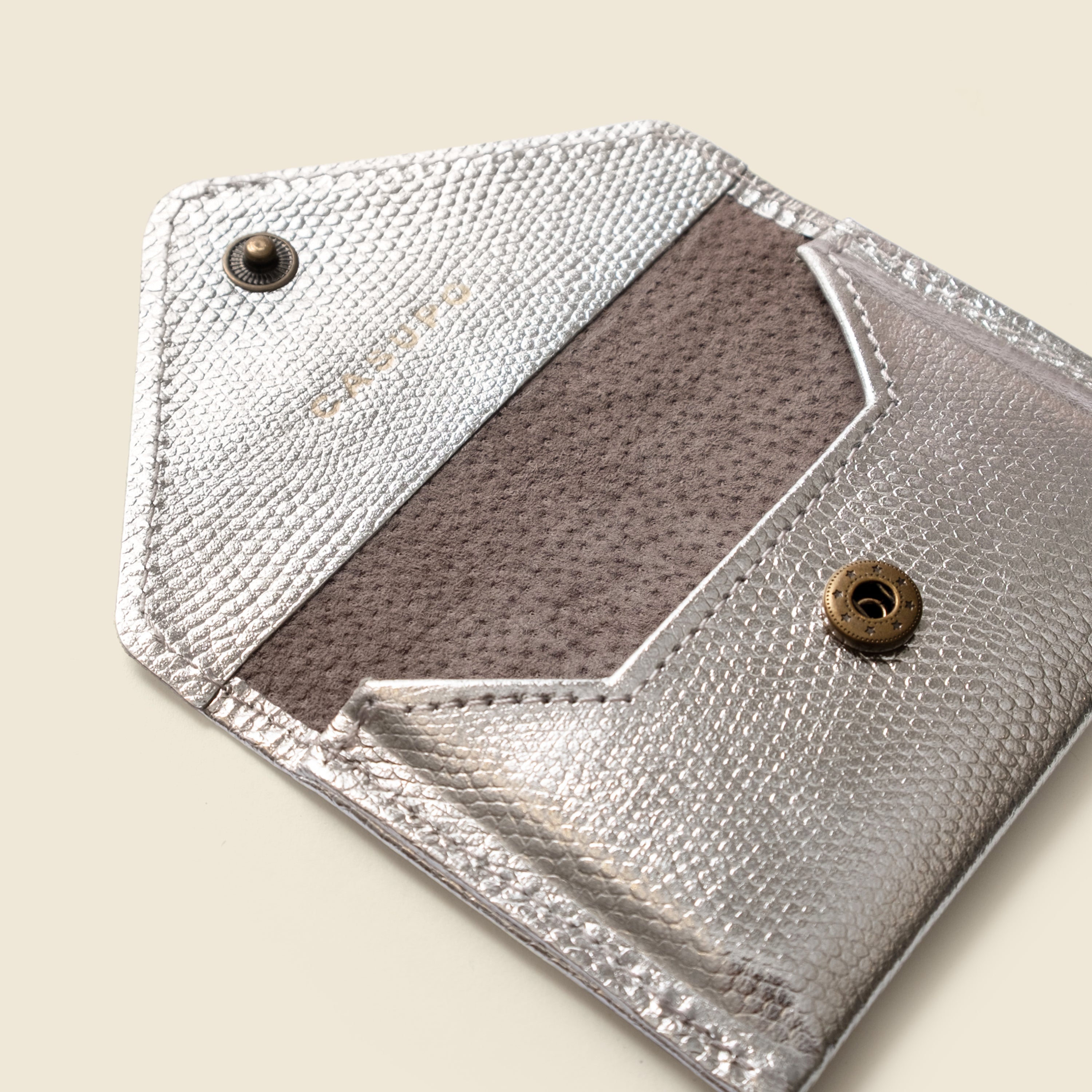 Close-up of a silver leather wallet with a textured flap on a beige background