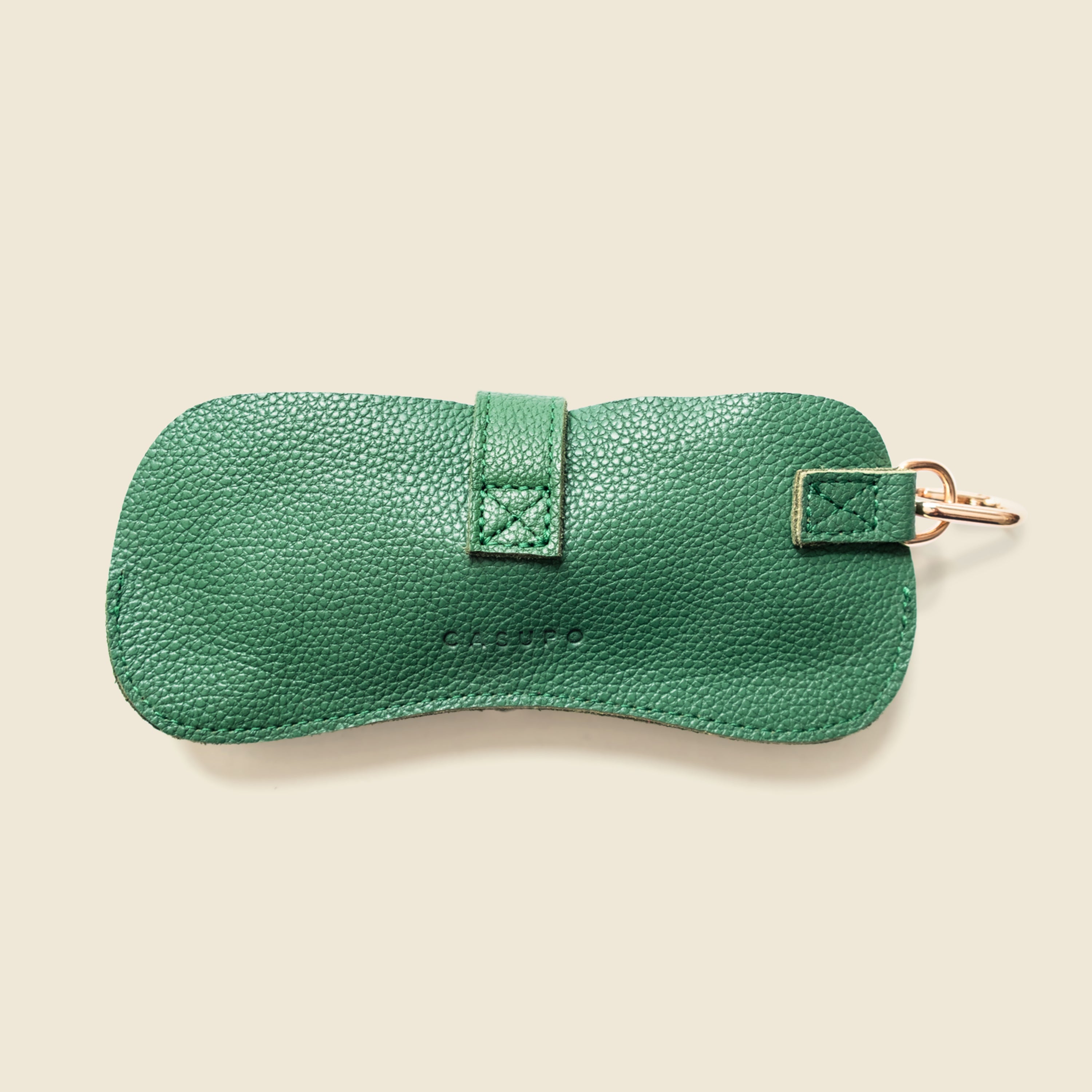 Green leather sunglasses case with gold clip on a beige background