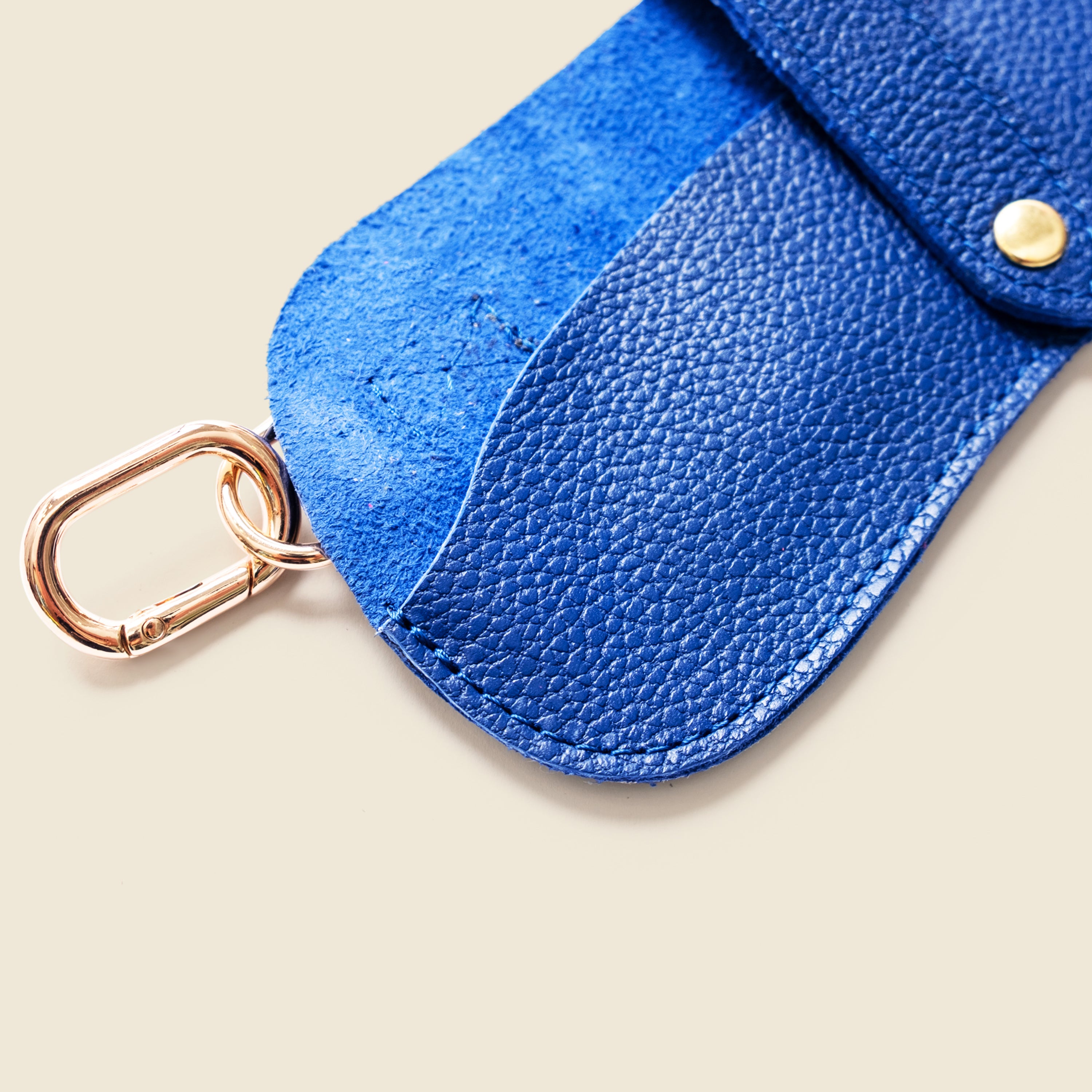 Blue leather key fob with a gold carabiner on a beige background