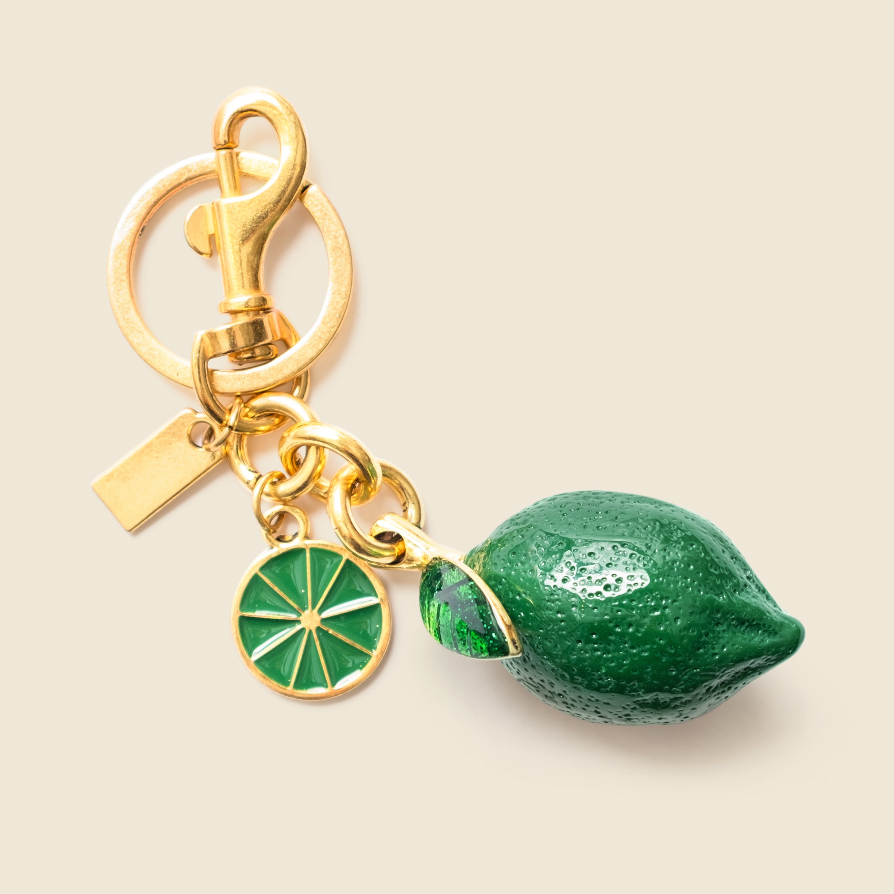 Gold keychain with green lemon charm on a beige background