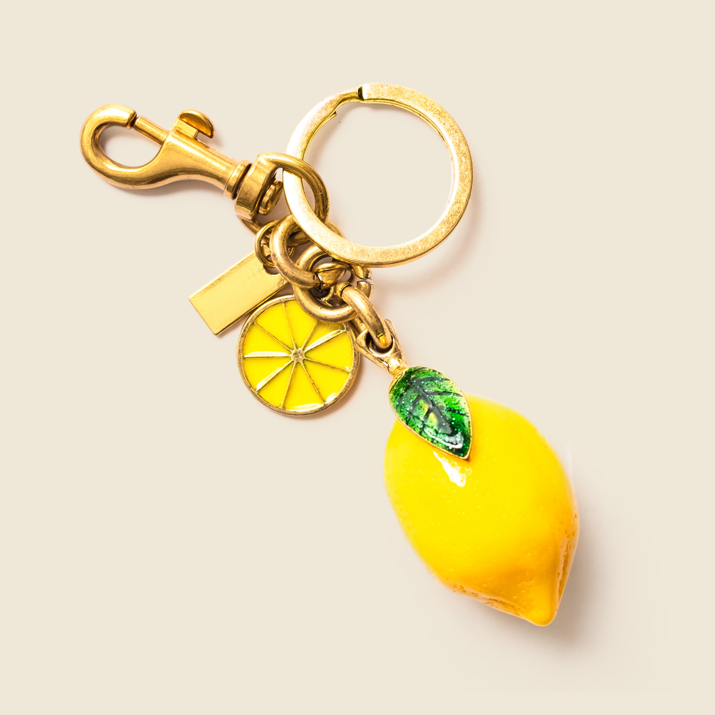 Gold keychain with lemon charm on a beige background