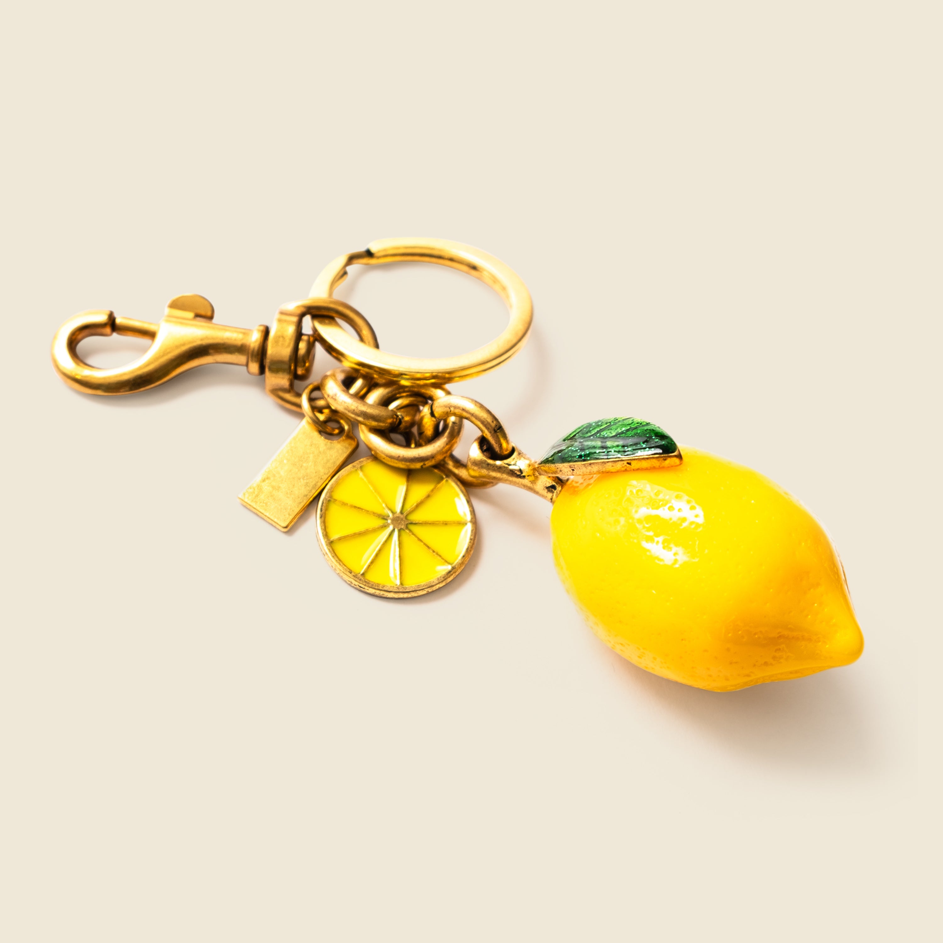 Gold keychain with lemon charm on a beige background