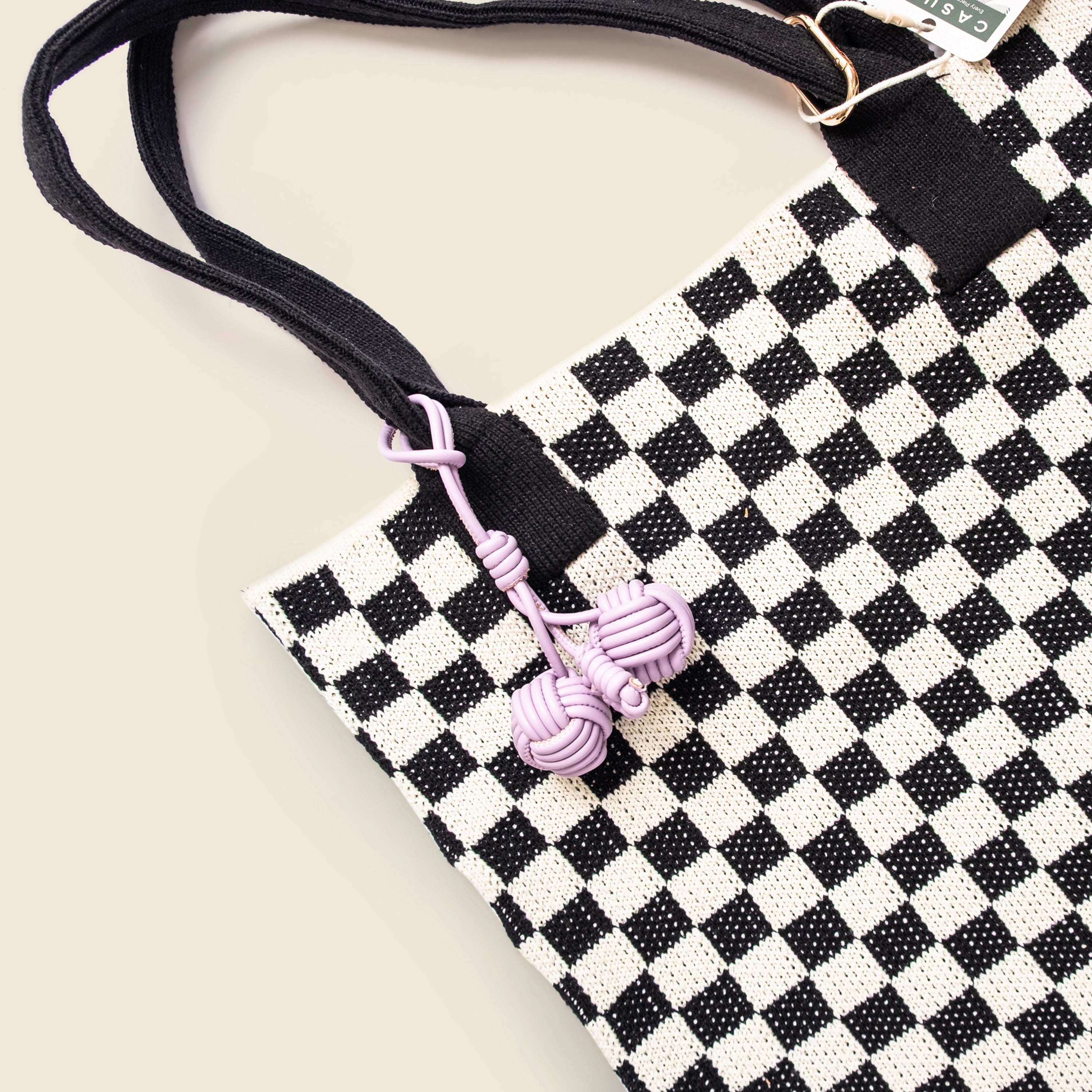 Black and white checkered bag with pink decorative charm on a beige background