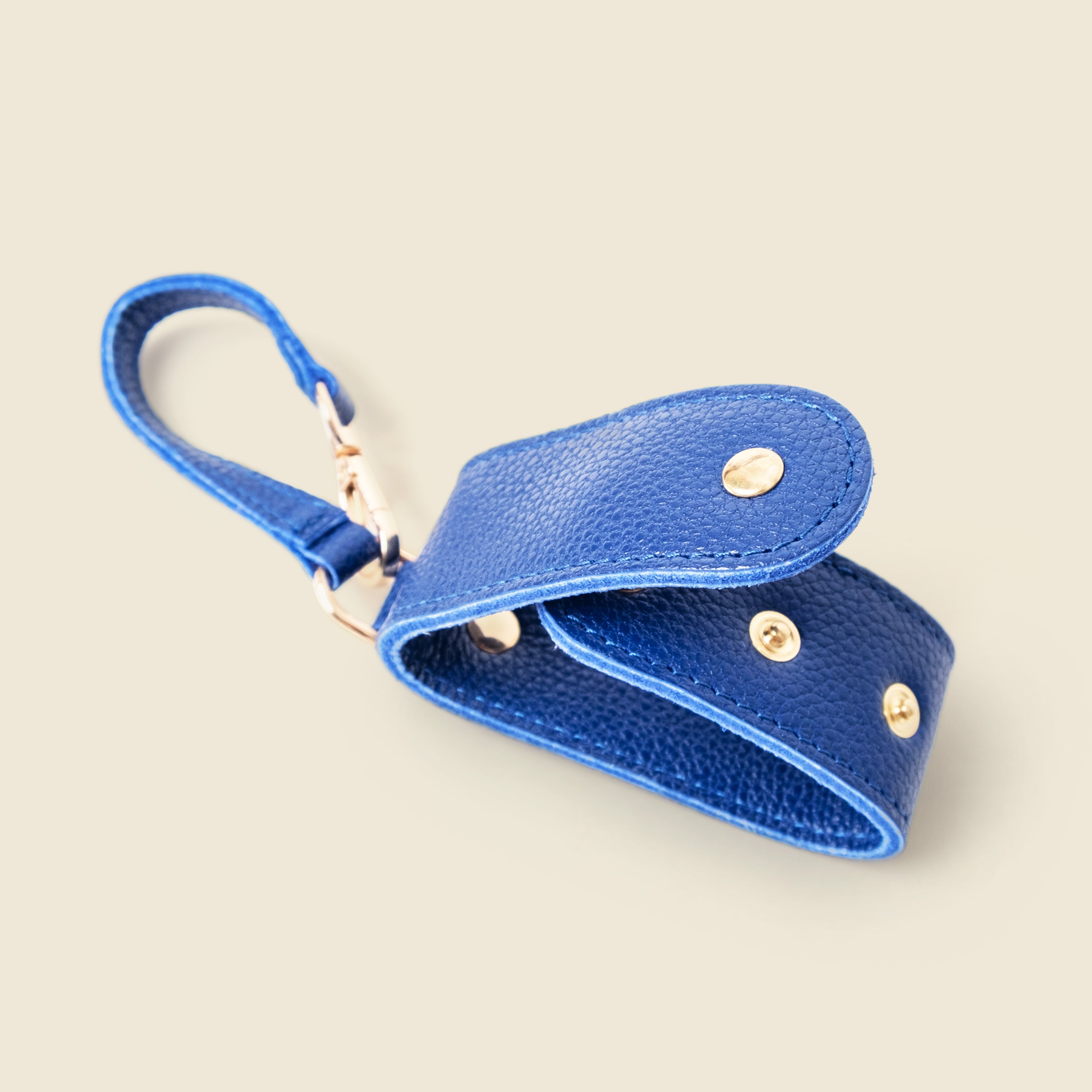 Blue leather keychain with gold accents on a beige background