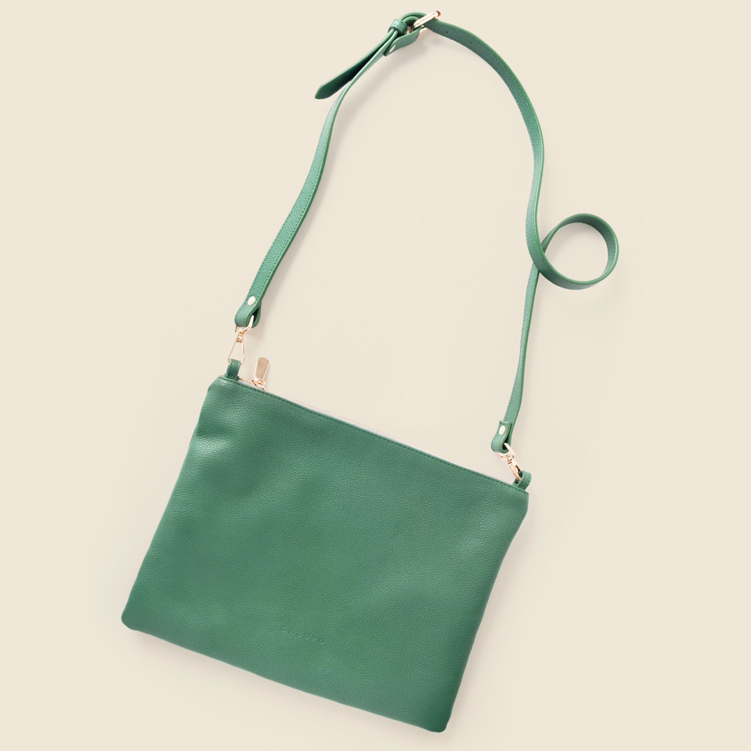 A green leather crossbody bag with a matching adjustable strap, displayed diagonally on a solid light beige background.