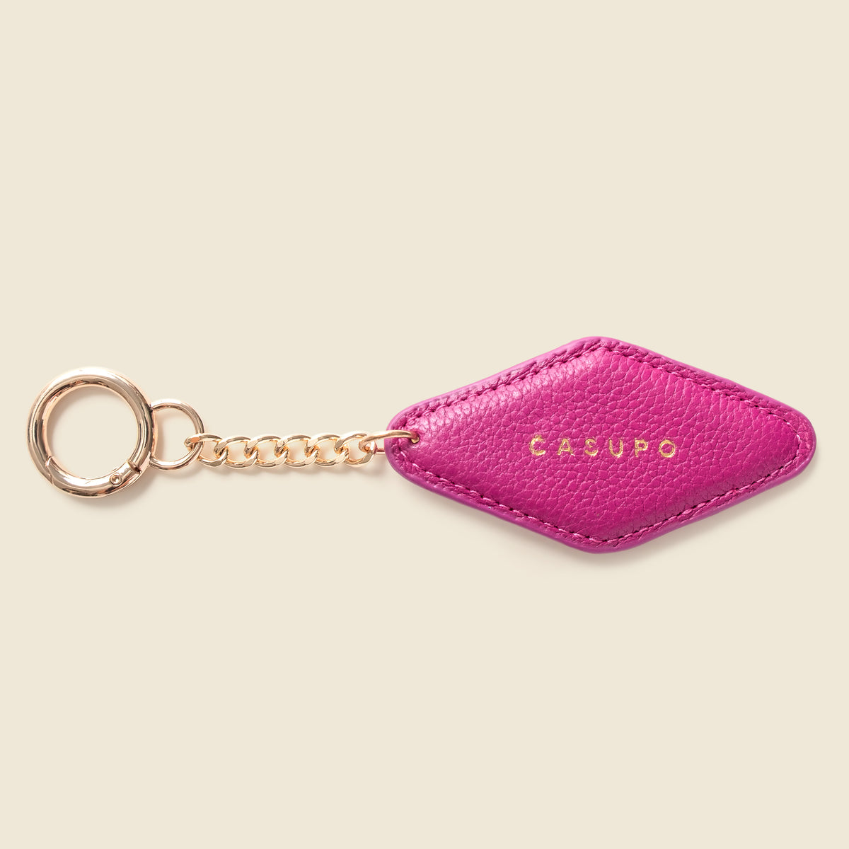 A bright pink textured leather keychain with a diamond-shaped tag, attached to a rose gold chain and key ring, featuring the brand name 'CASUPO' in gold lettering on the tag, set against a solid light beige background.
