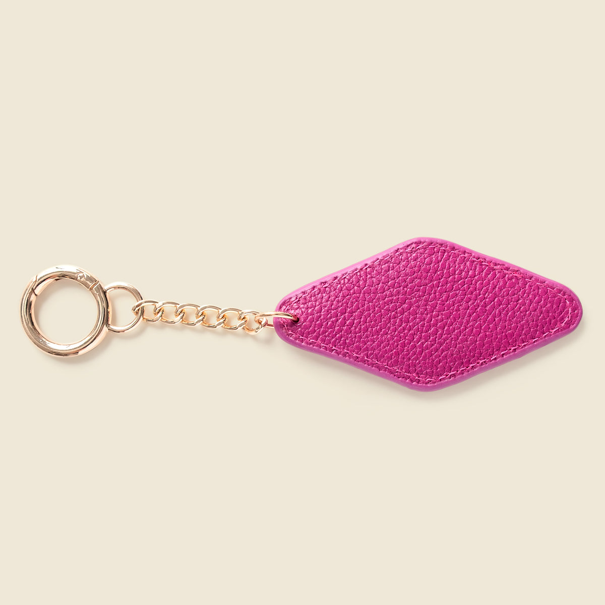 A bright pink textured leather keychain with a gold-tone metal ring and chain, shown on a solid light beige background.
