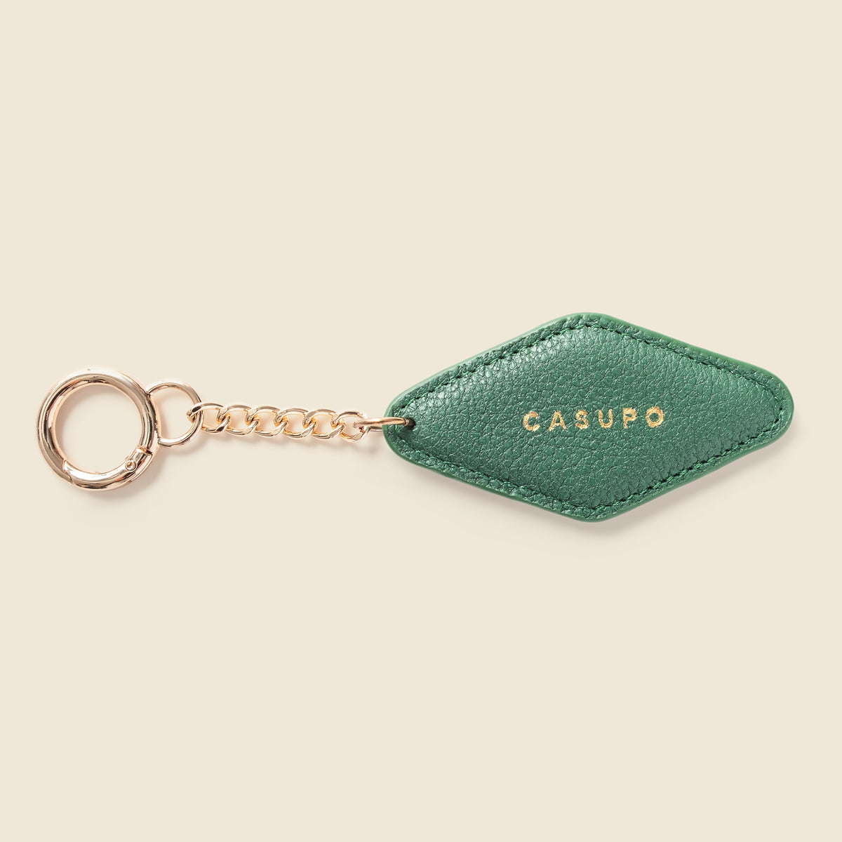A green textured leather keychain with a gold-tone chain and key ring, featuring the brand name 'CASUPO' in gold lettering on the leather tab, set against a solid cream background.