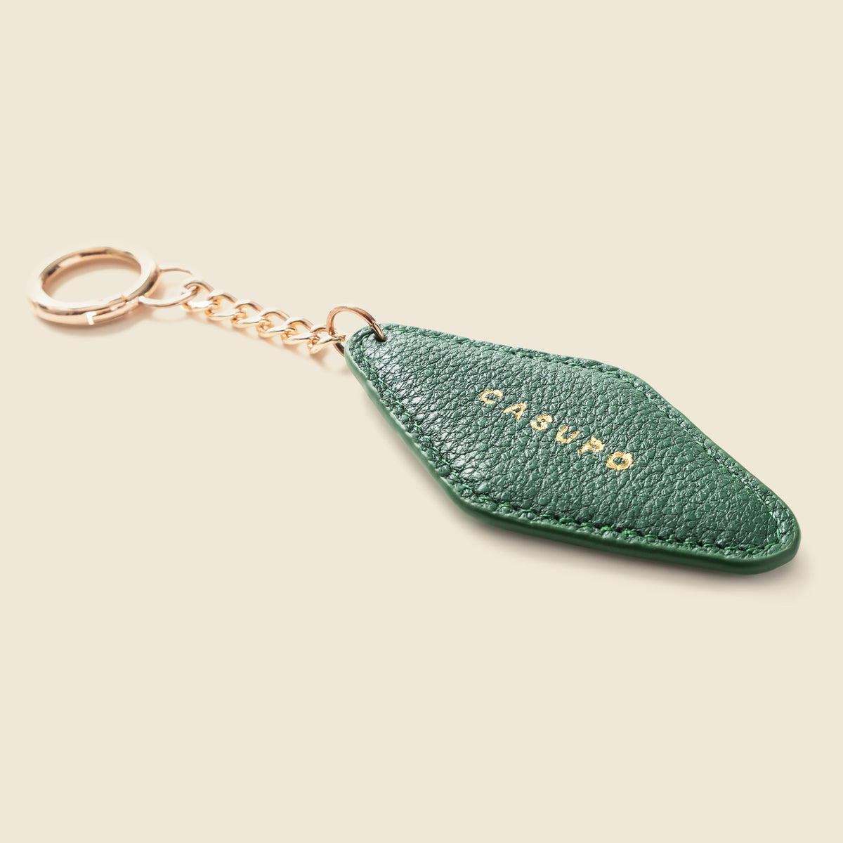 A green textured leather keychain with a diamond-shaped tag and gold-tone hardware, featuring the brand name 'CASUFO' in gold lettering, set against a solid beige background.